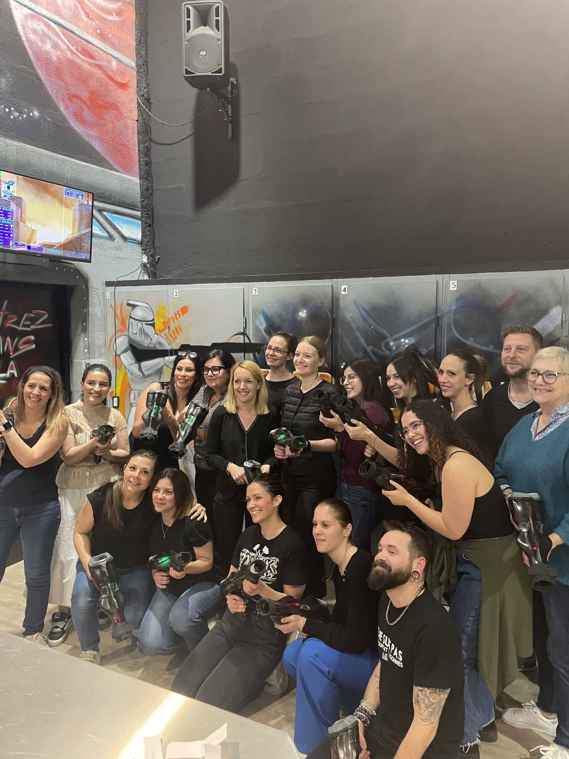 Groupe souriant posant avec du matériel de laser tag lors d'une activité de team building ludique en salle.