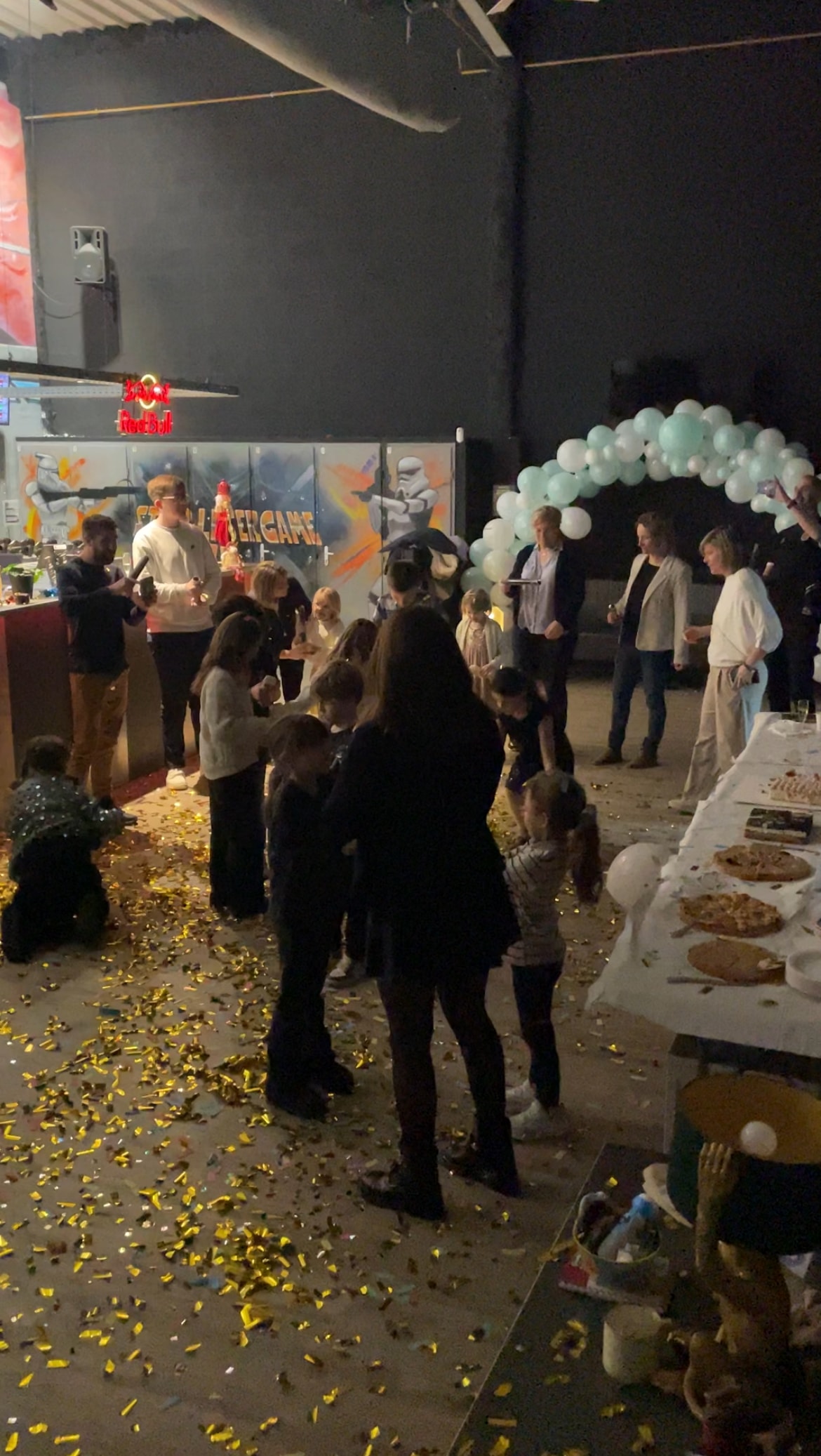 Fête d'anniversaire au Lasergame avec confettis dorés, murale Star Wars et buffet de pizzas pour enfants et adultes.