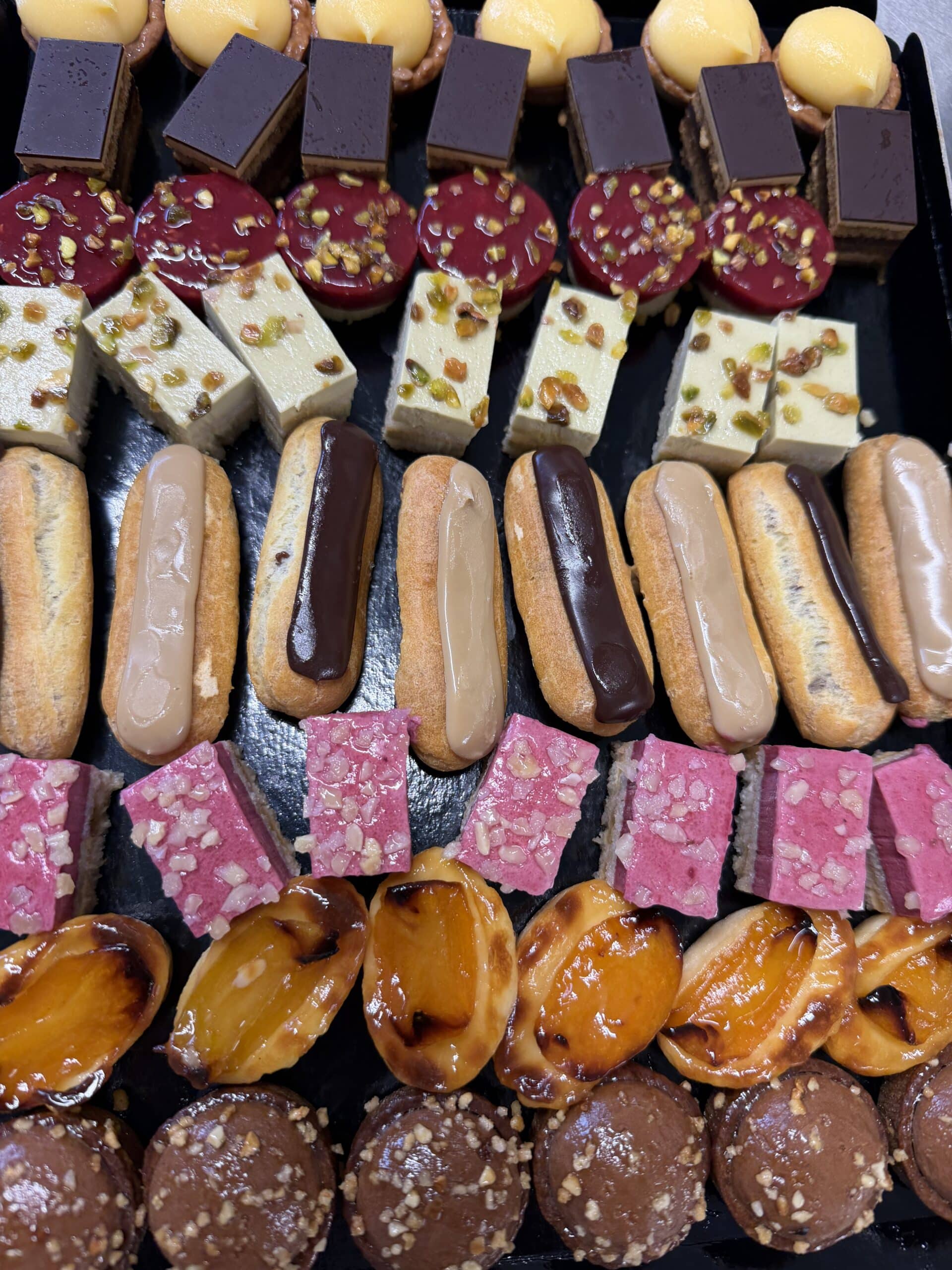 Assortiment de mignardises sucrées : mini éclairs, tartelettes, entremets pistache et gâteaux chocolatés sur un plateau.