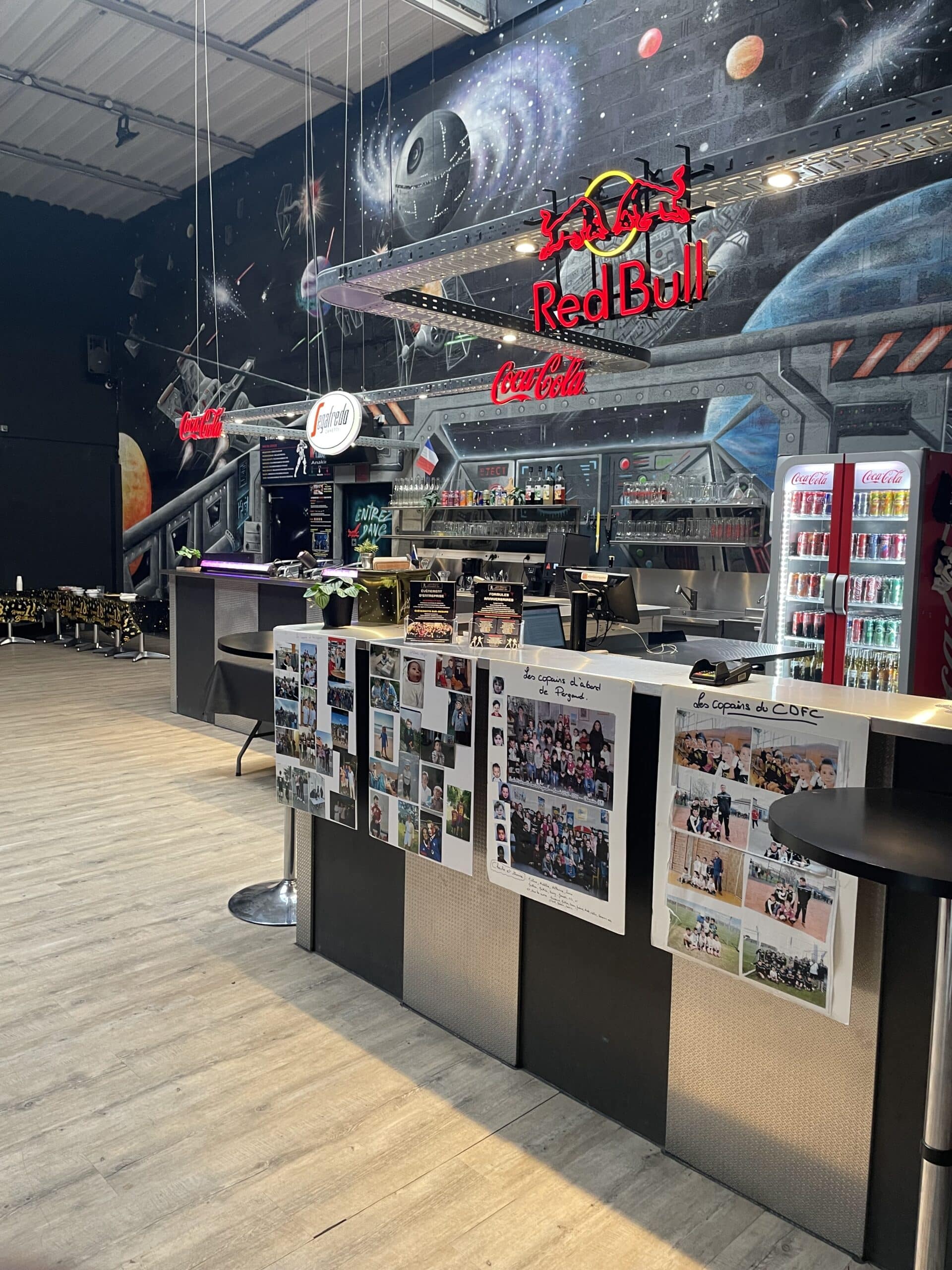 Bar à thème Star Wars avec fresque spatiale, logos Red Bull et Coca-Cola lumineux sur un comptoir décoré de photos.