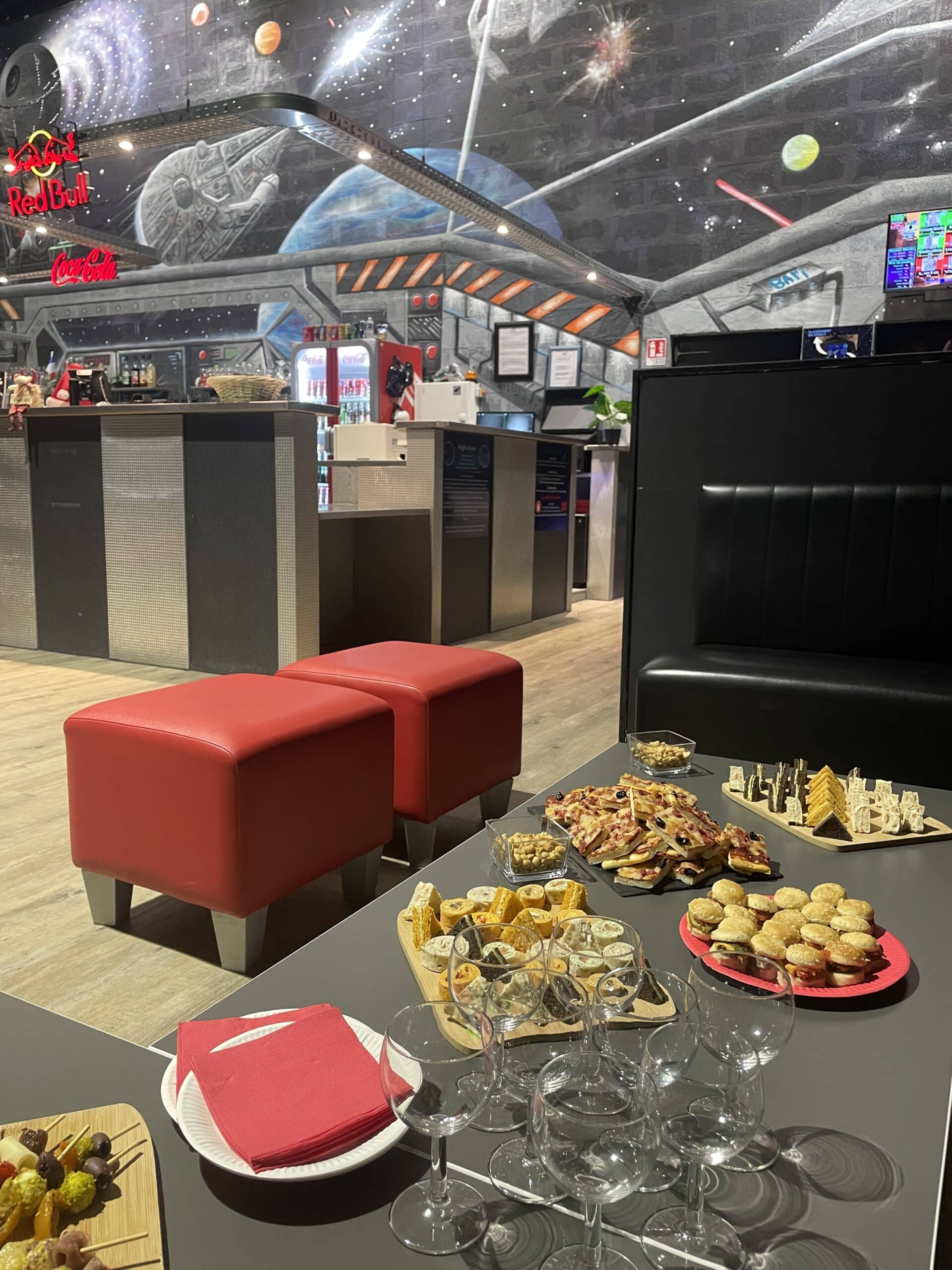 Buffet dînatoire avec amuses-bouches, poufs rouges et fresque murale Star Wars Red Bull Coca-Cola dans un bar.