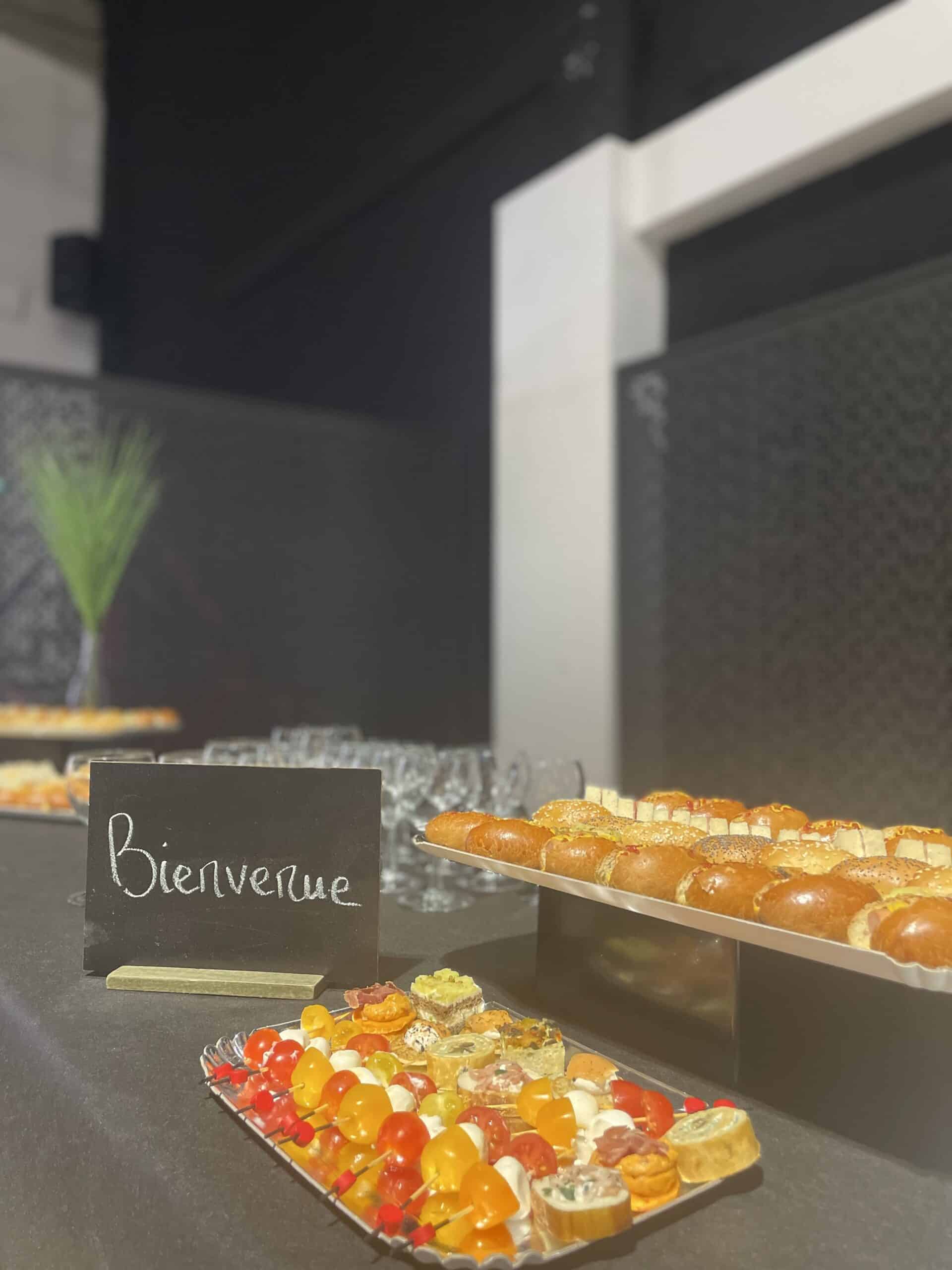 Buffet traiteur avec amuse-bouches variés et panneau 'Bienvenue' lors d'un cocktail dînatoire élégant.
