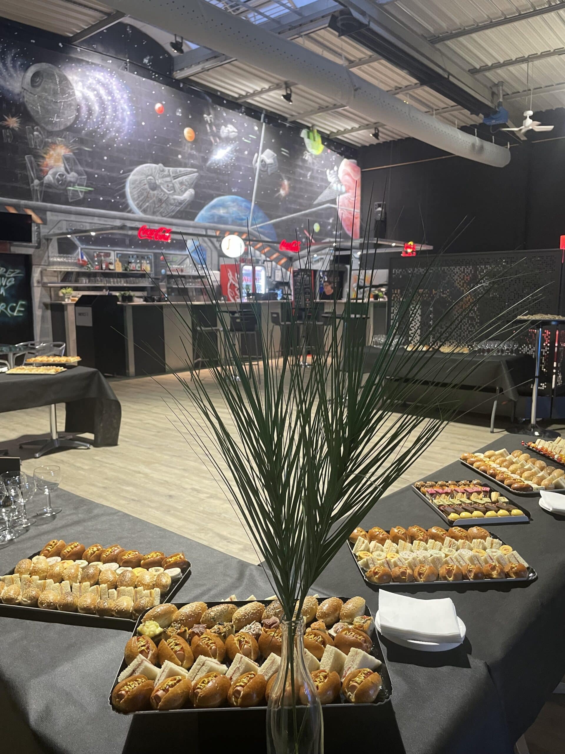 Buffet traiteur événementiel thème Star Wars avec amuse-bouches variés devant une grande fresque galactique murale.