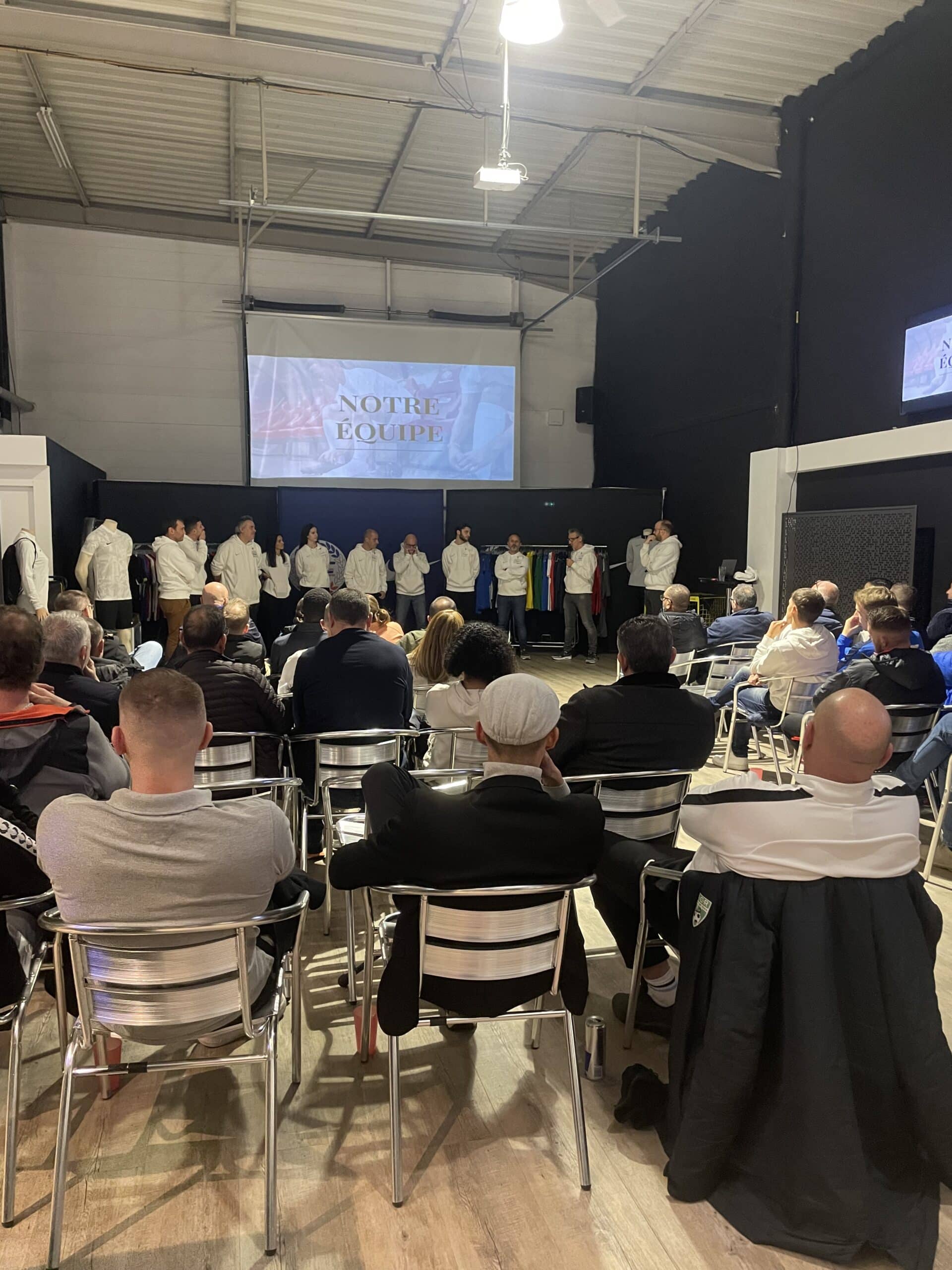 Conférence événementielle NOTRE ÉQUIPE devant un public assis dans un hangar lors d'une présentation d'entreprise.