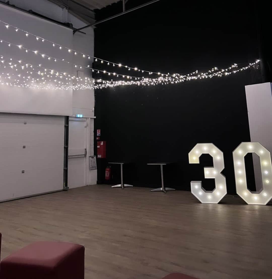 Décoration d'anniversaire avec grands chiffres 30 lumineux et guirlandes dans une salle de fête moderne.