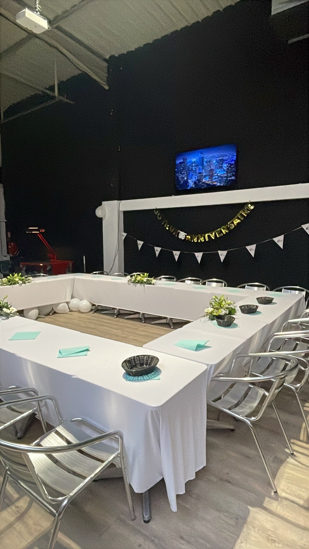 Table en U avec nappes blanches, fleurs et bannière Joyeux Anniversaire pour une réception festive en salle.