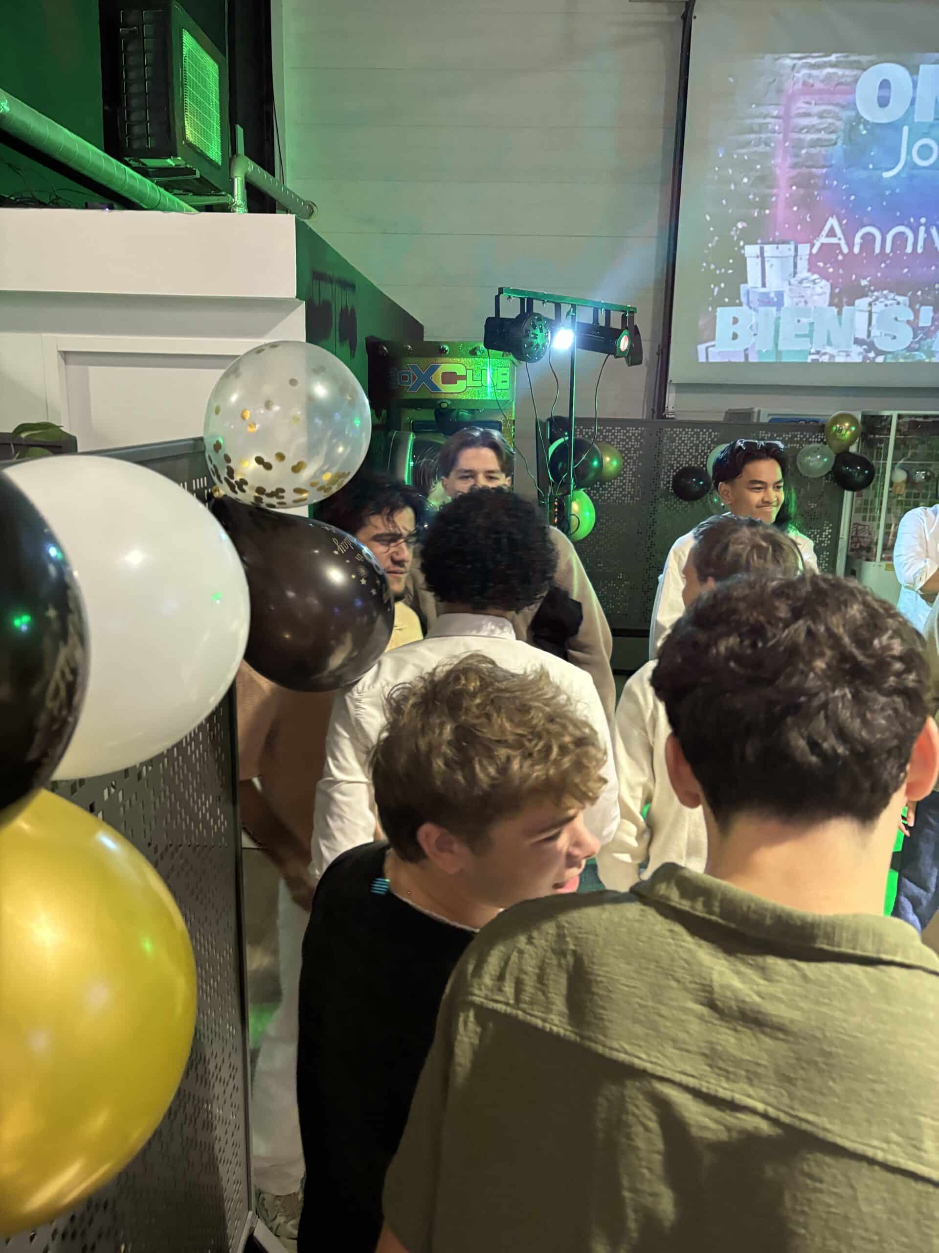 Jeunes lors d'une fête d'anniversaire avec ballons dorés et blancs devant un écran projetant Anniv BIENS.