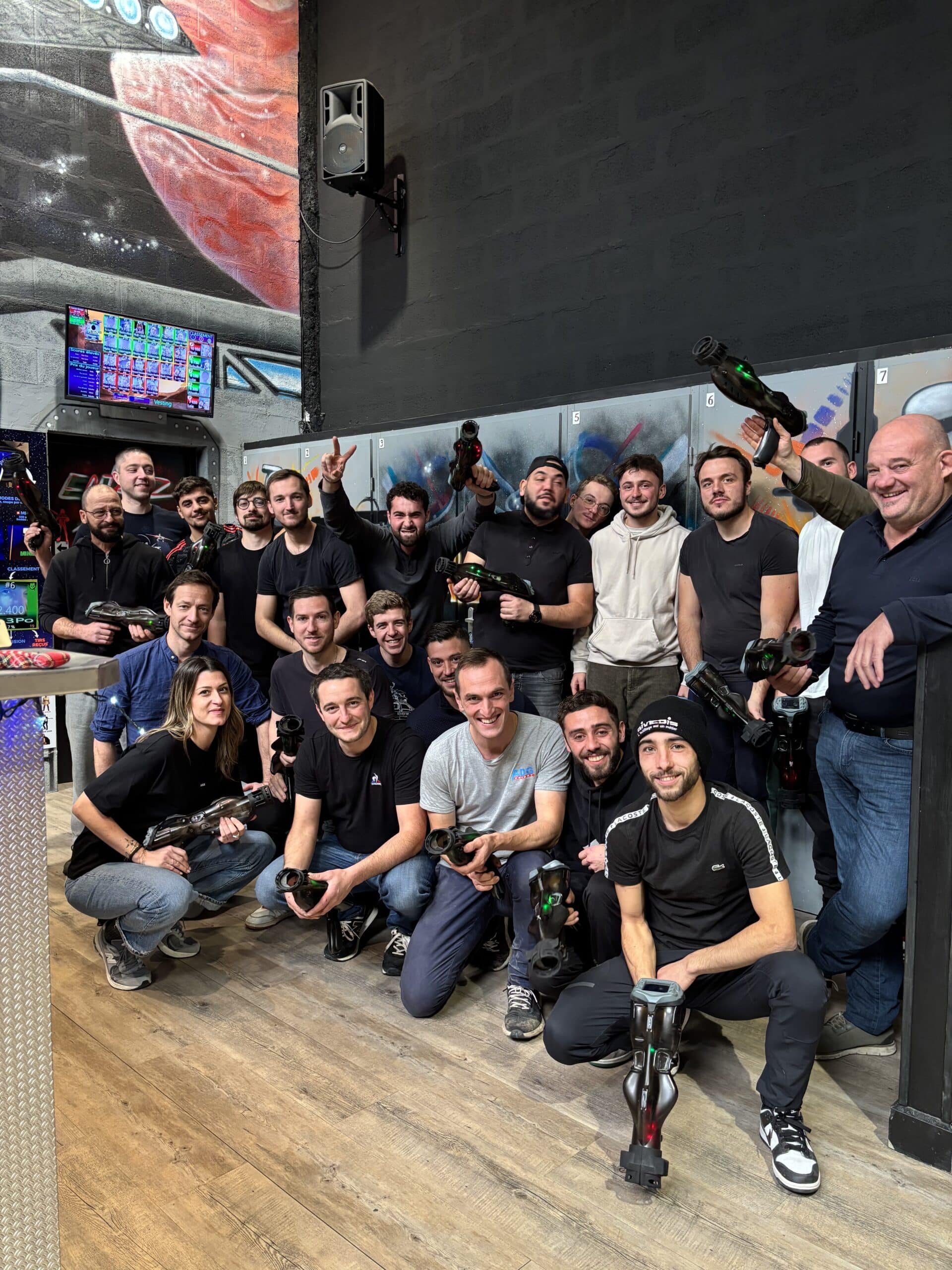 Équipe souriante posant avec matériel de laser tag dans une salle de jeu urbaine et colorée.