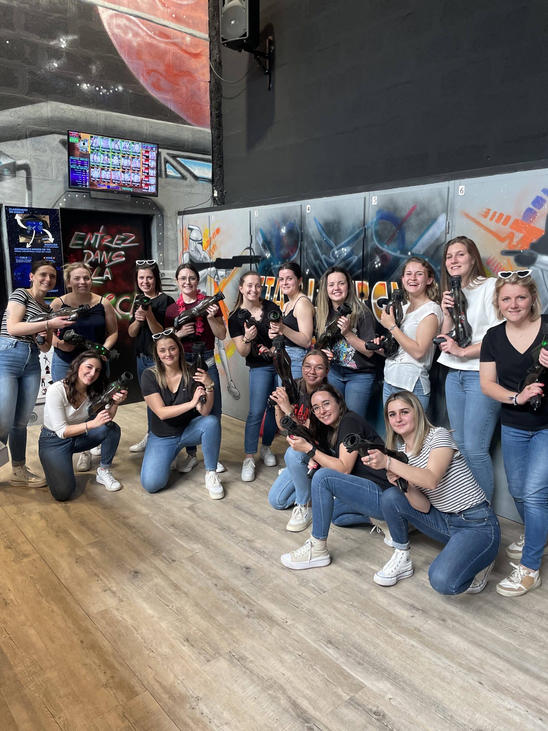 Groupe de femmes souriantes avec pistolets laser game devant un mur de graffiti lors d'une sortie entre amies.