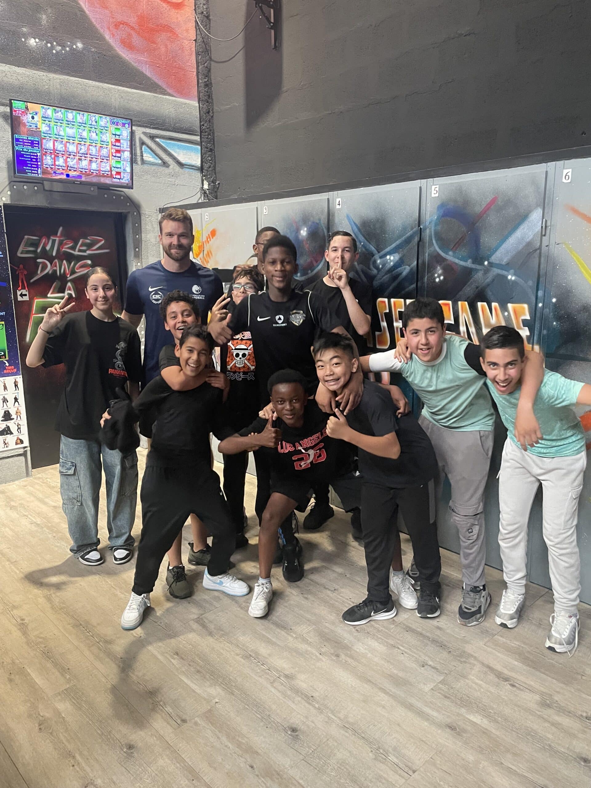 Groupe de jeunes souriants et coach devant des casiers de laser game. Ambiance festive et dynamique.