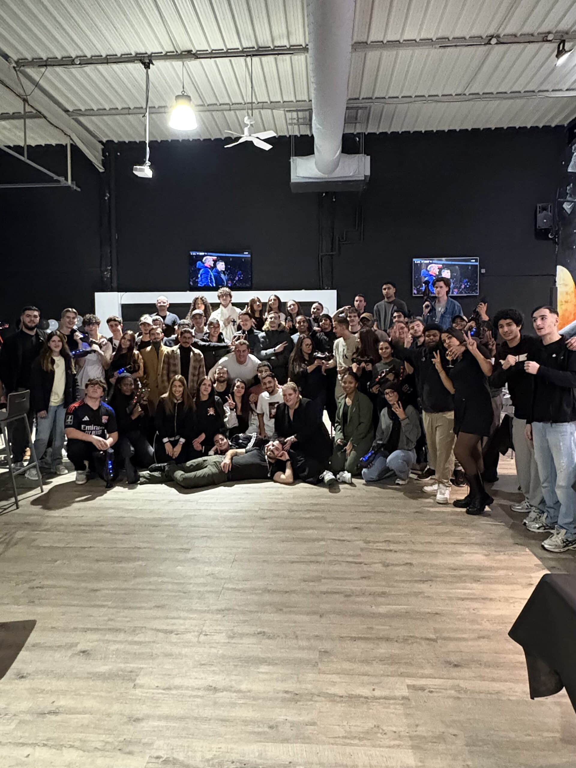 Grand groupe de jeunes posant avec enthousiasme dans une salle de laser tag, certains tenant leur équipement de jeu.