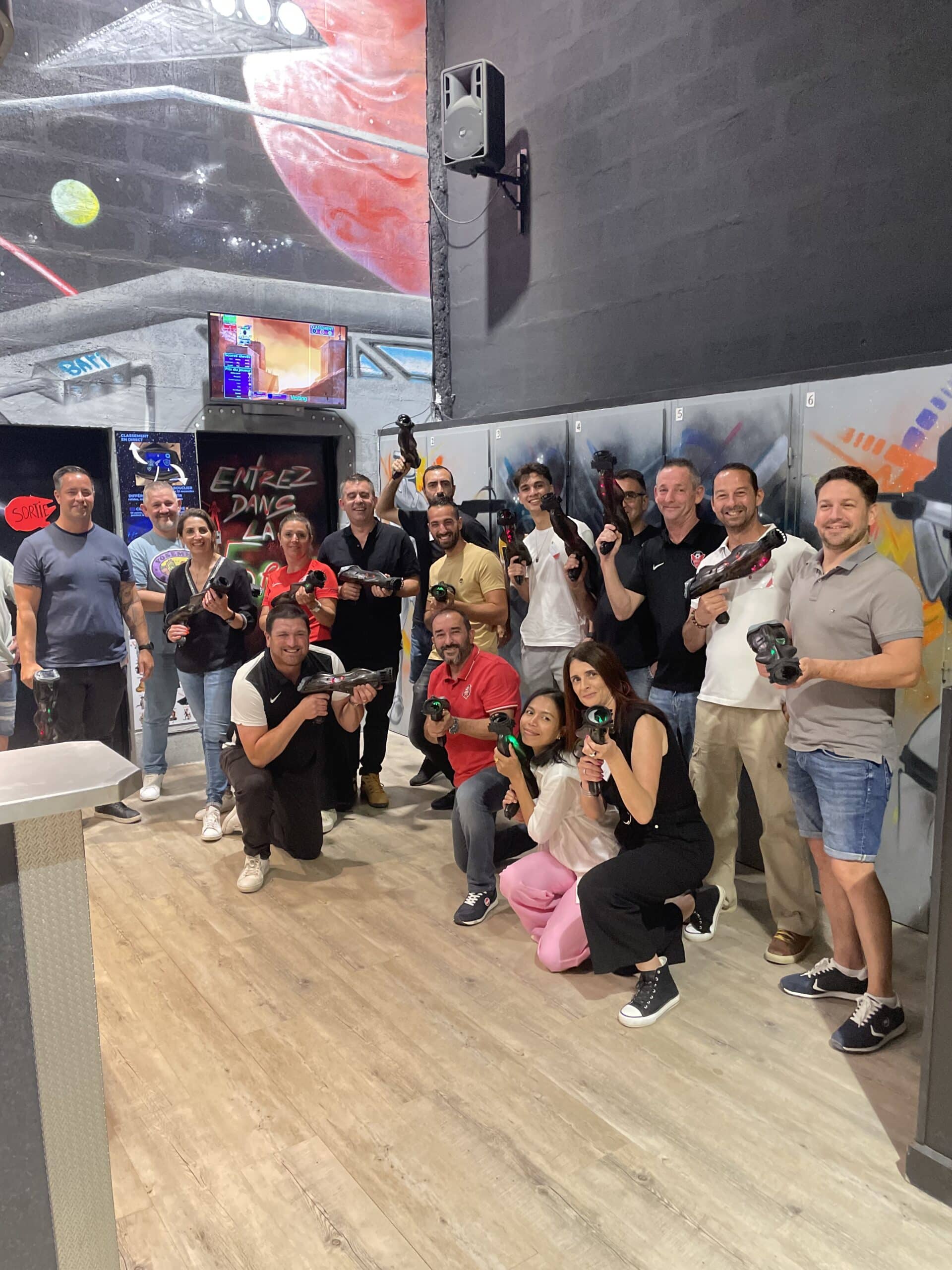 Groupe souriant posant avec pistolets laser tag devant un décor spatial pour une session de team building.