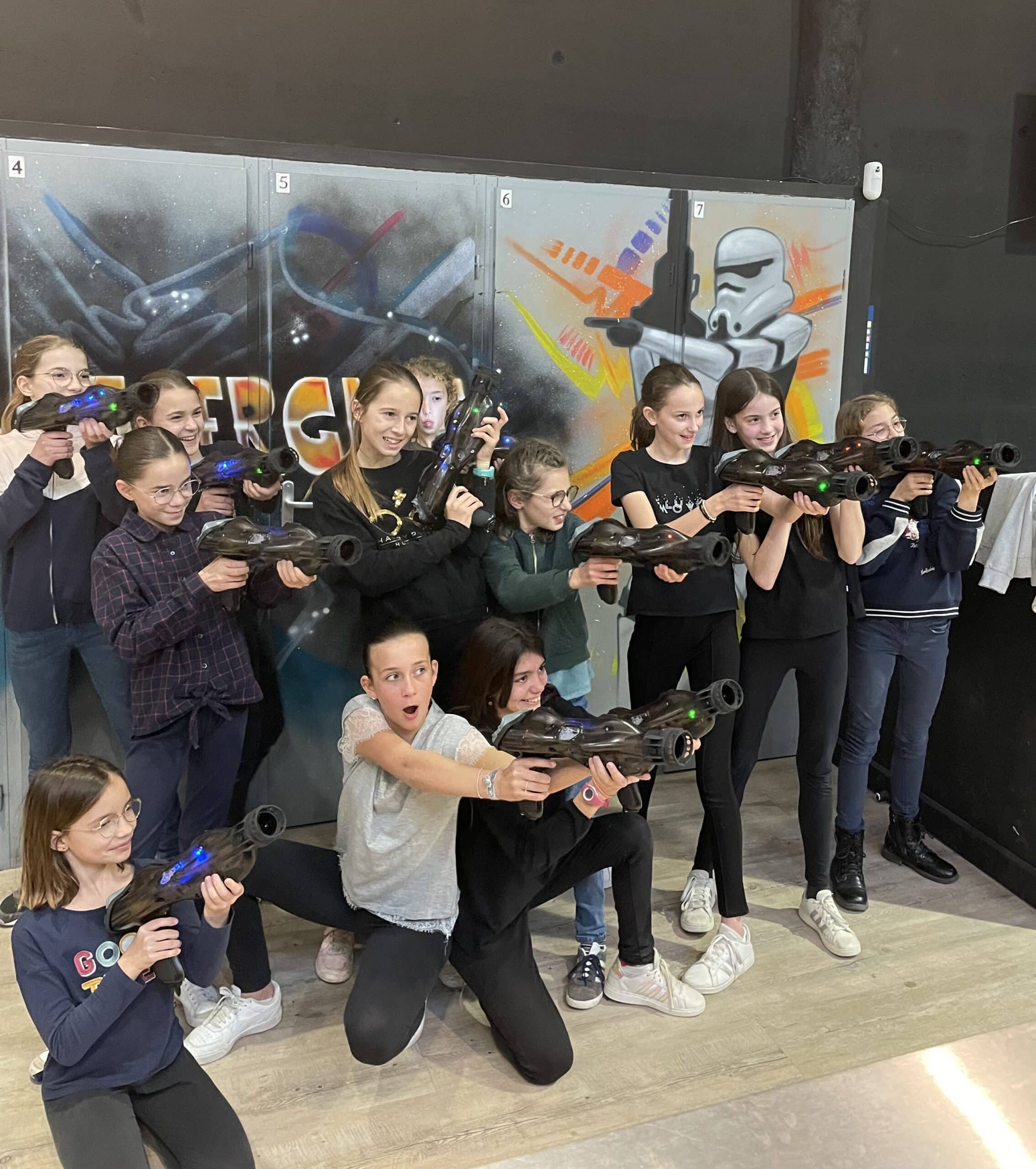 Groupe de filles posant avec des pistolets laser tag devant un graffiti de Stormtrooper lors d'un anniversaire.