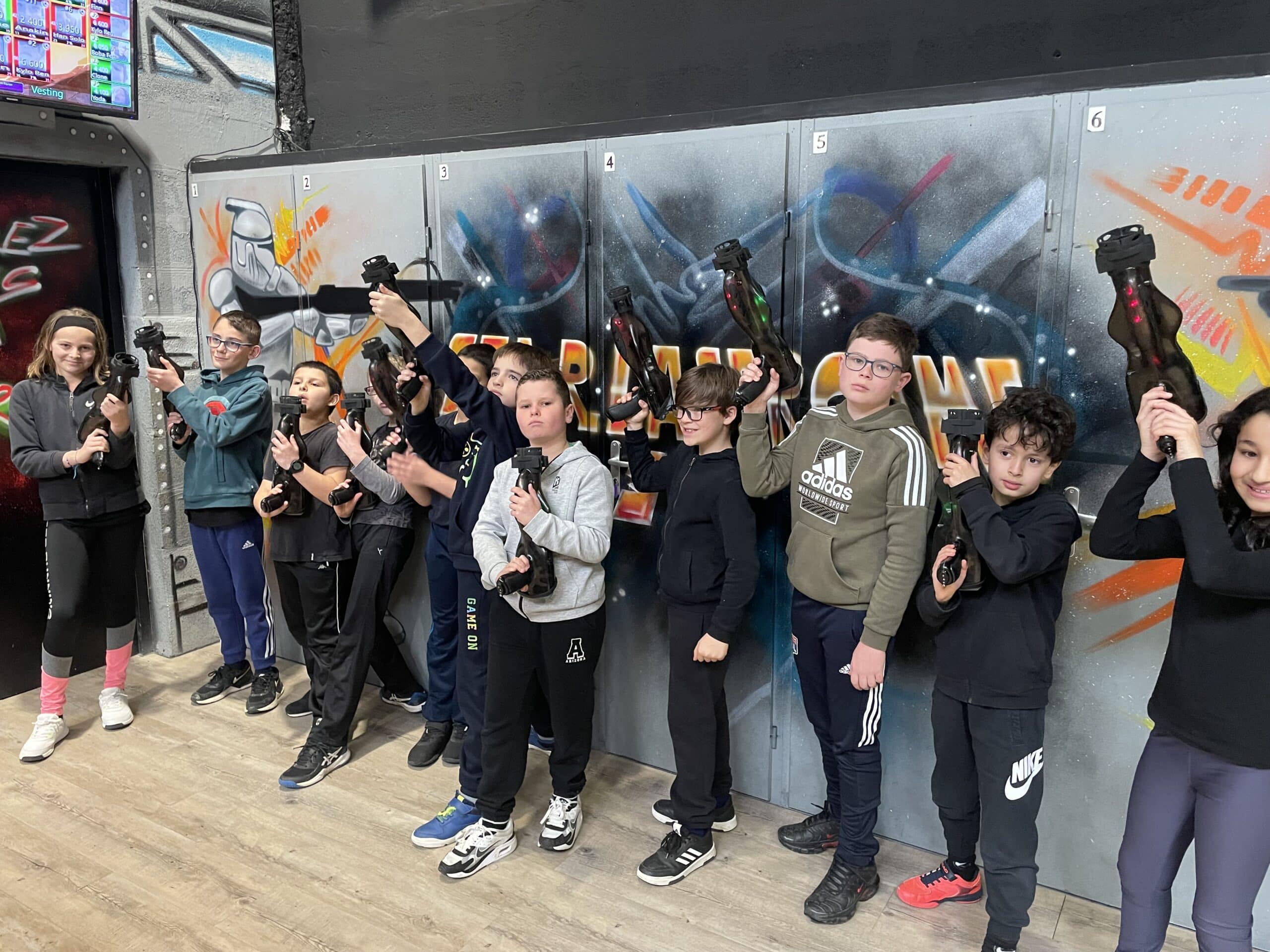 Groupe d'enfants avec équipement laser tag devant des casiers tagués Star Wars, souriants et prêts pour l'action.