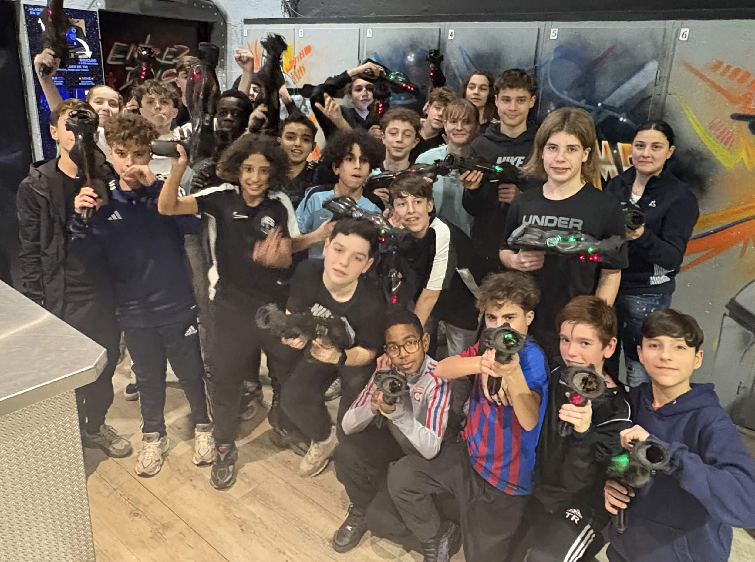 Groupe de jeunes souriants posant avec des pistolets laser tag devant des casiers dans un centre de loisirs.