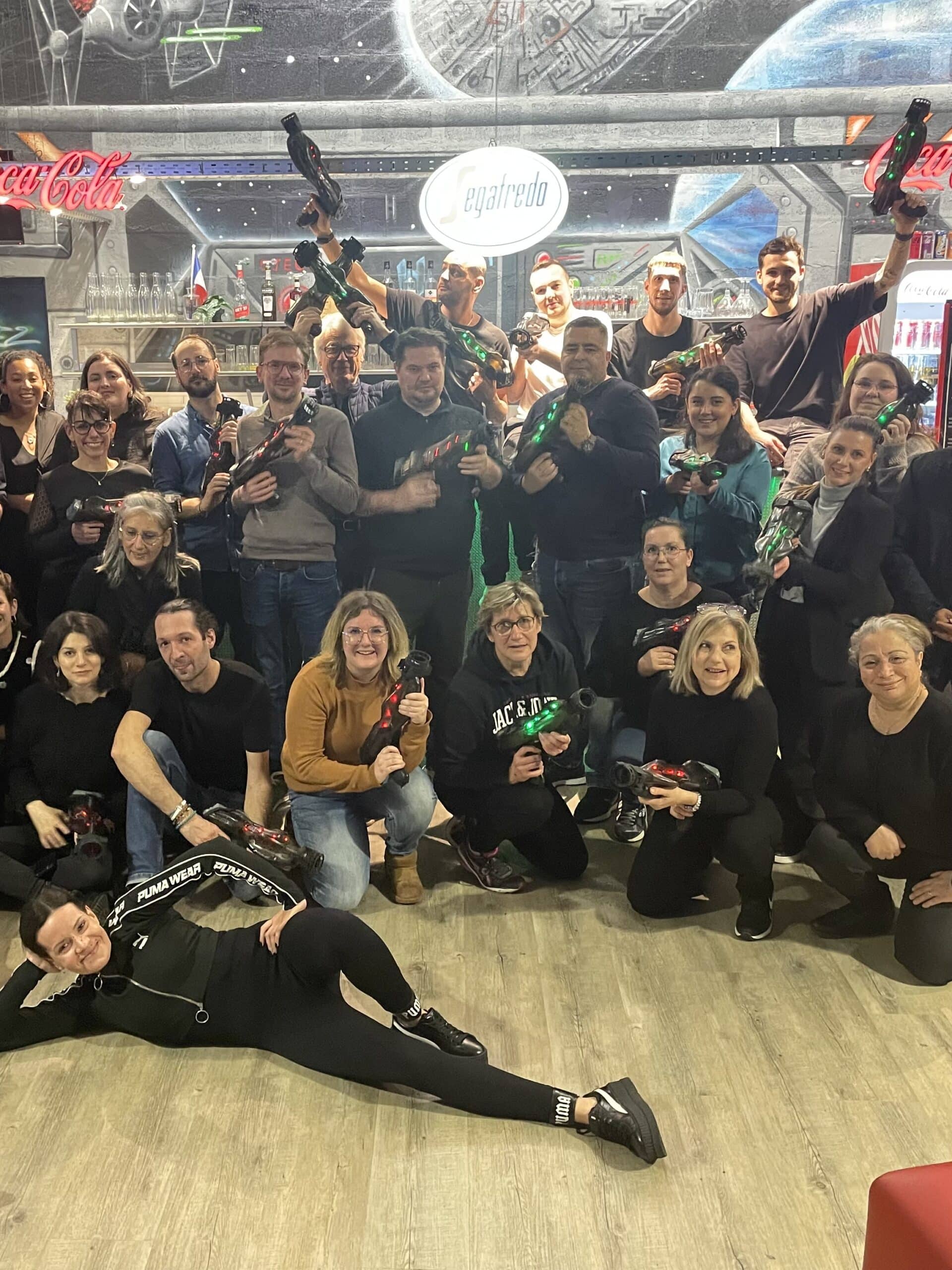 Groupe joyeux en session laser tag posant avec des blasters devant un décor Star Wars et l'enseigne Segafredo.