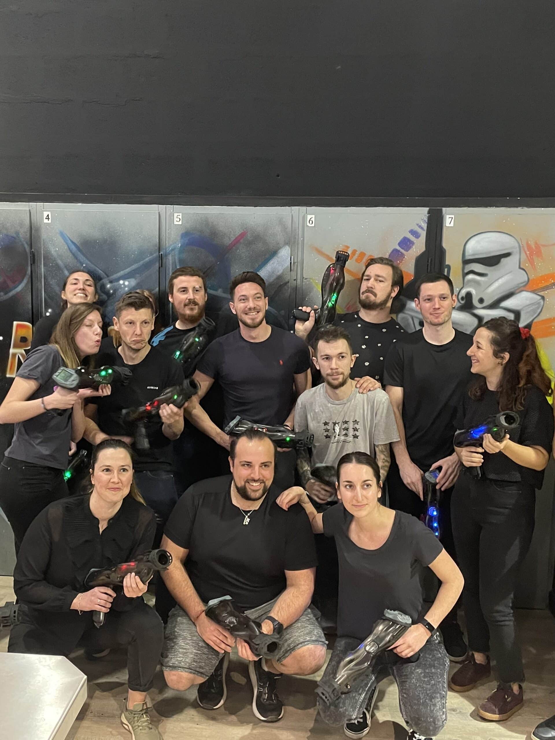 Groupe souriant avec pistolets de laser tag devant un mur de graffitis Star Wars lors d'un team building.