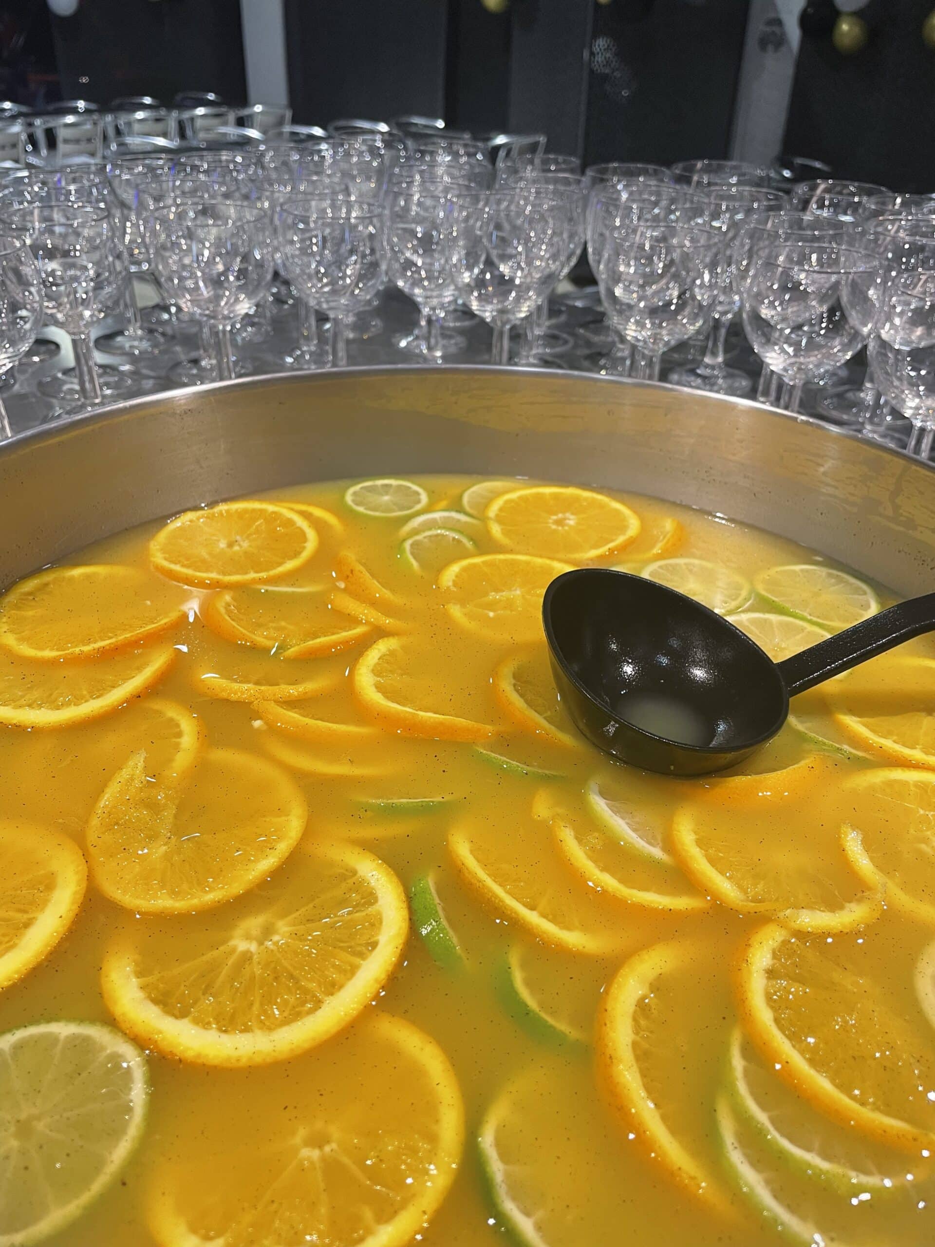 Punch aux agrumes avec tranches d'oranges et citrons verts dans un grand bol, entouré de verres en cristal.