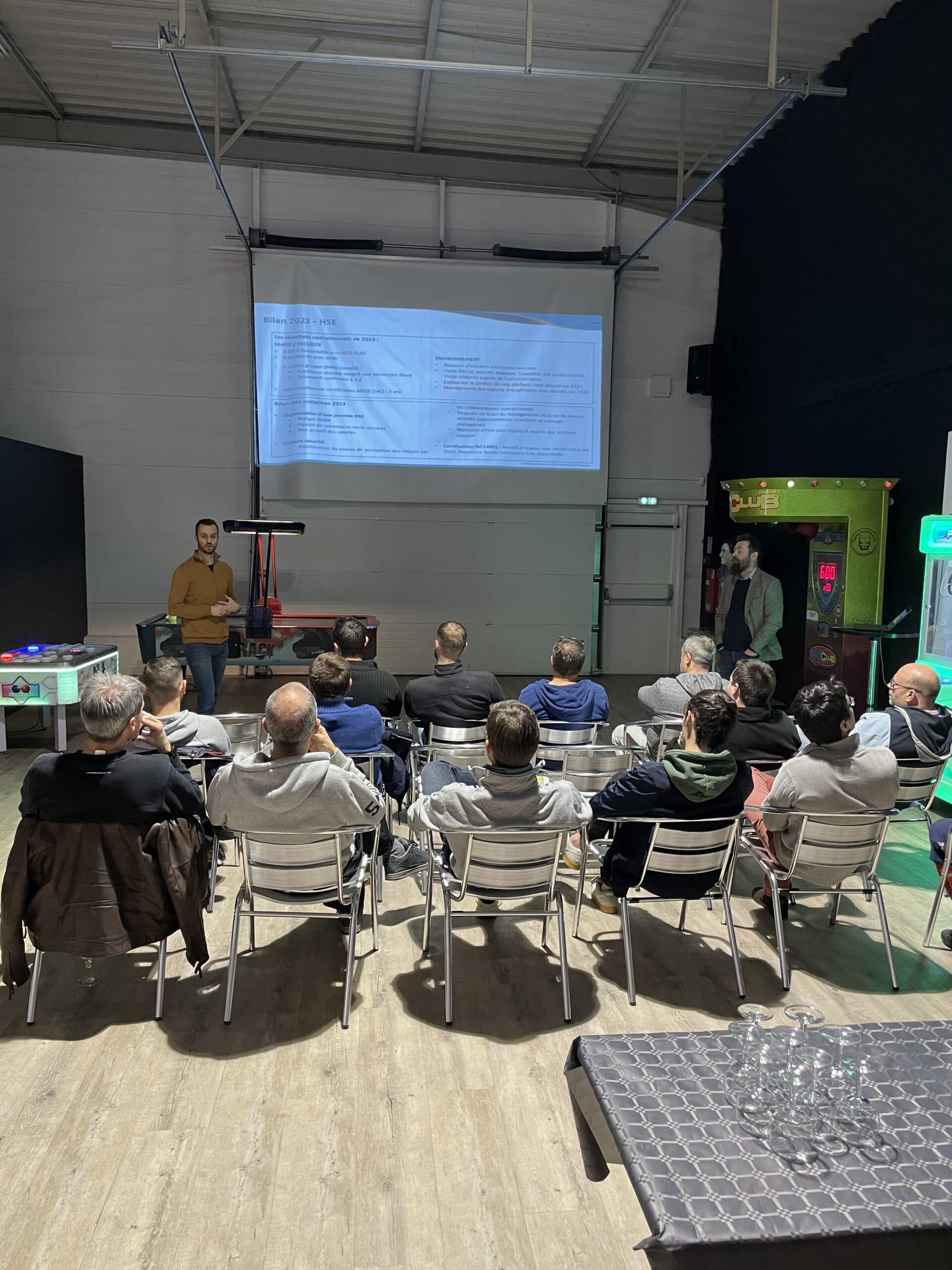 Présentation du Bilan 2023 - HSE lors d'une réunion d'équipe dans une salle avec jeux d'arcade et air hockey.
