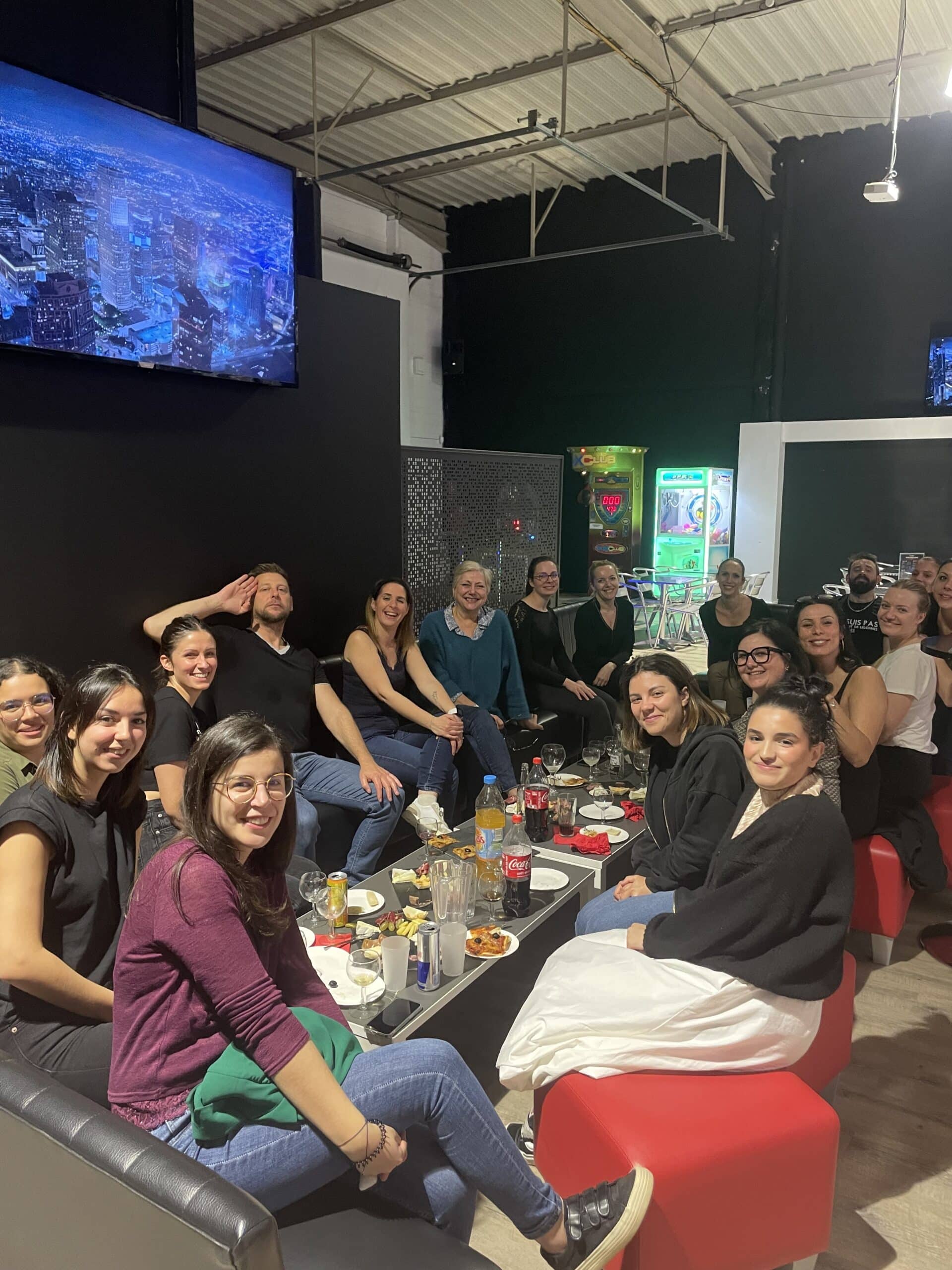 Groupe d'amis souriants lors d'une soirée conviviale autour d'un apéritif dans un bar lounge avec jeux d'arcade.