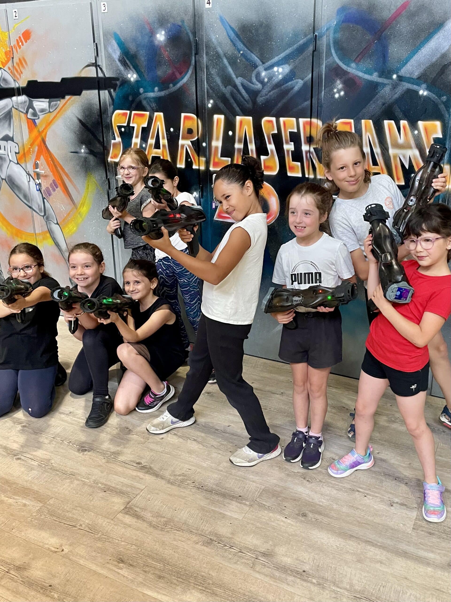 Groupe d'enfants avec pistolets laser devant un mur STAR LASER GAME lors d'une activité d'anniversaire.