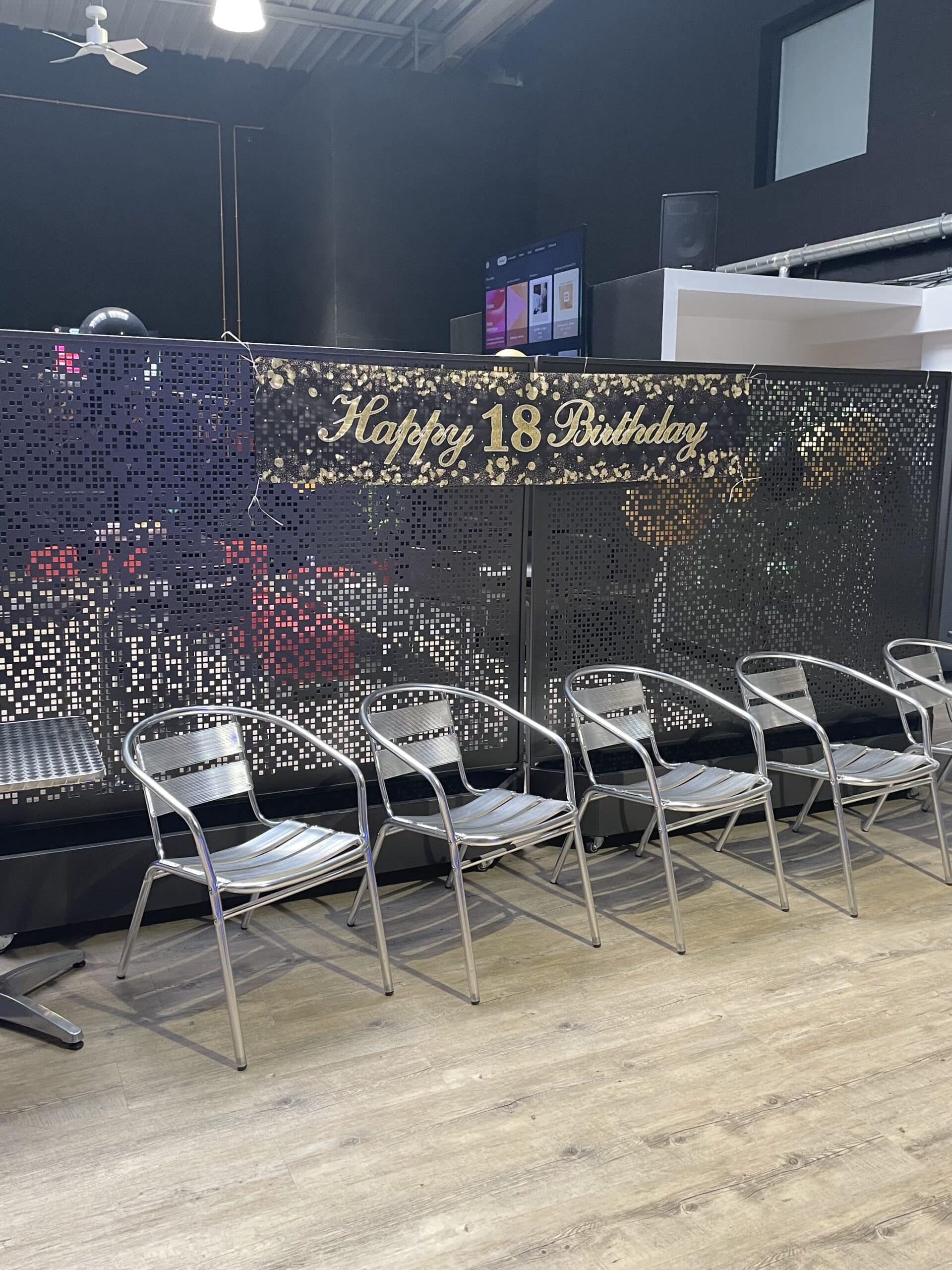 Banderole Happy 18 Birthday dorée accrochée au-dessus d'une rangée de chaises en métal argenté dans un salon moderne.