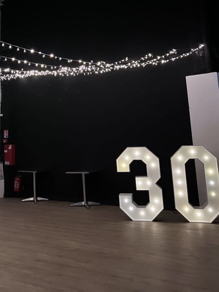 Grands chiffres 30 lumineux sur parquet avec guirlandes, idéal pour une décoration d'anniversaire chic.