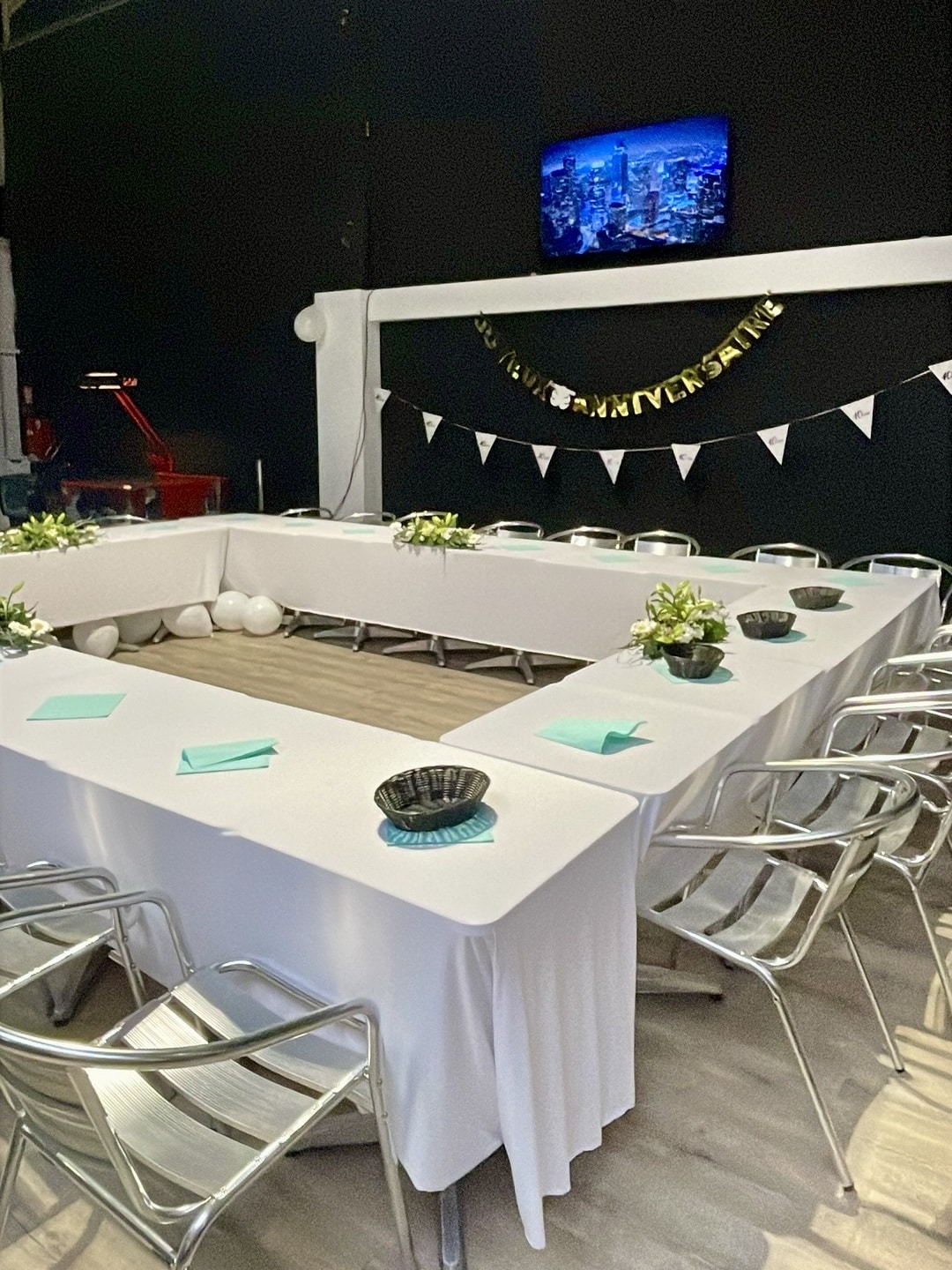 Décoration de salle d'anniversaire avec tables en U, fleurs blanches et bannière dorée Joyeux Anniversaire.