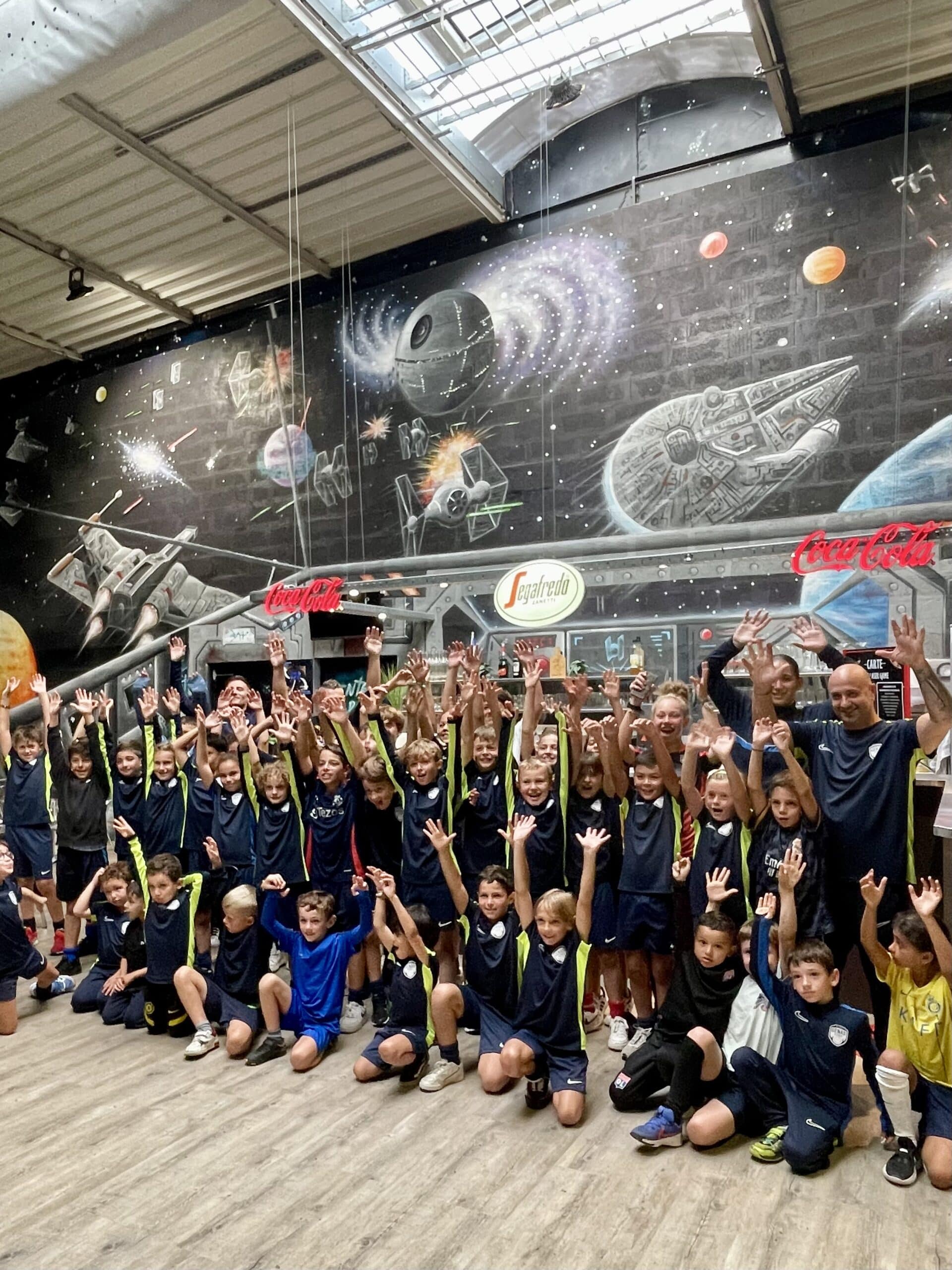 Jeunes footballeurs célébrant devant une fresque Star Wars géante avec X-wing et Faucon Millénium.