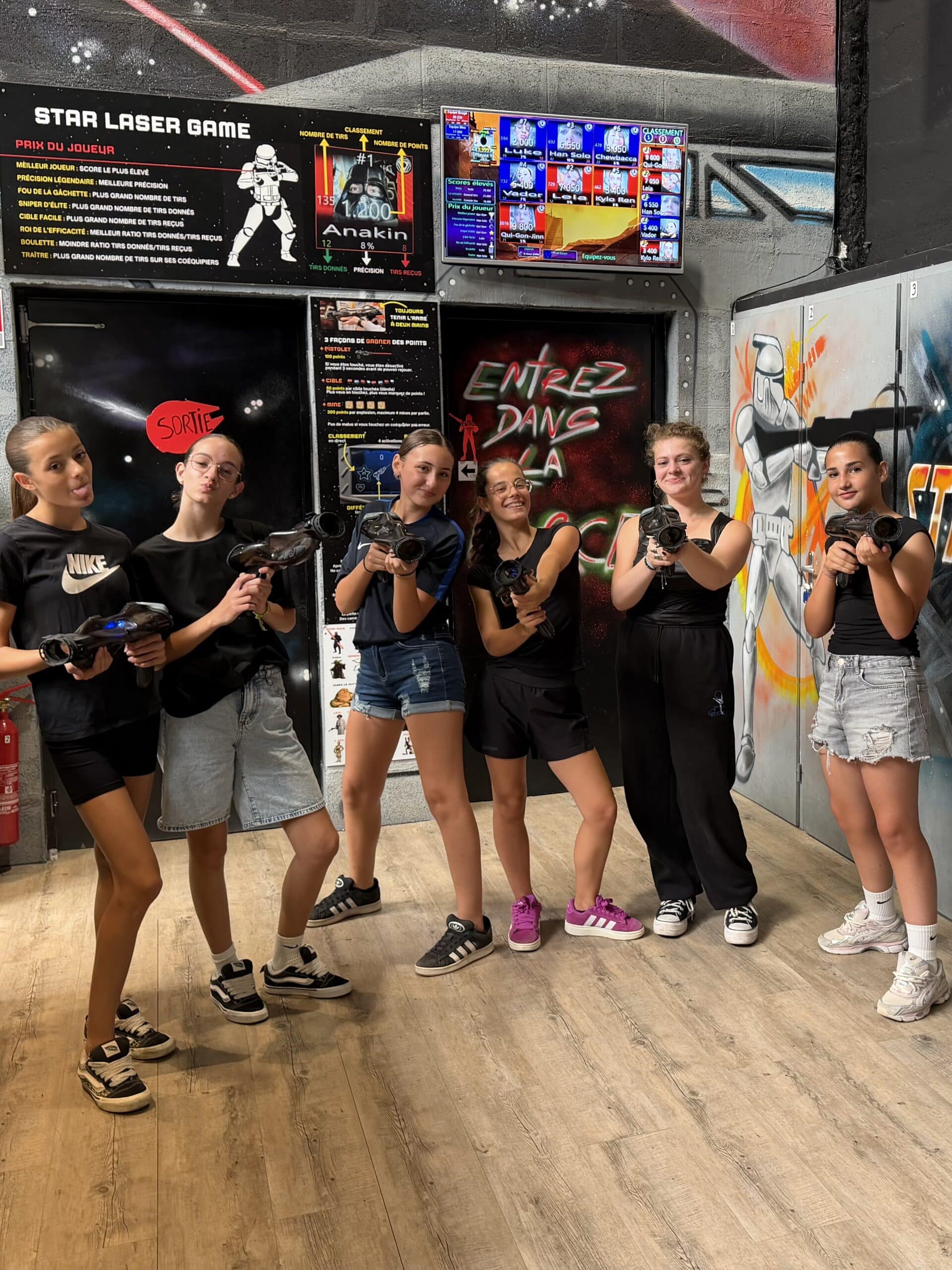 Six adolescentes posent avec des pistolets laser au Star Laser Game, ambiance Star Wars avec tableaux de scores.