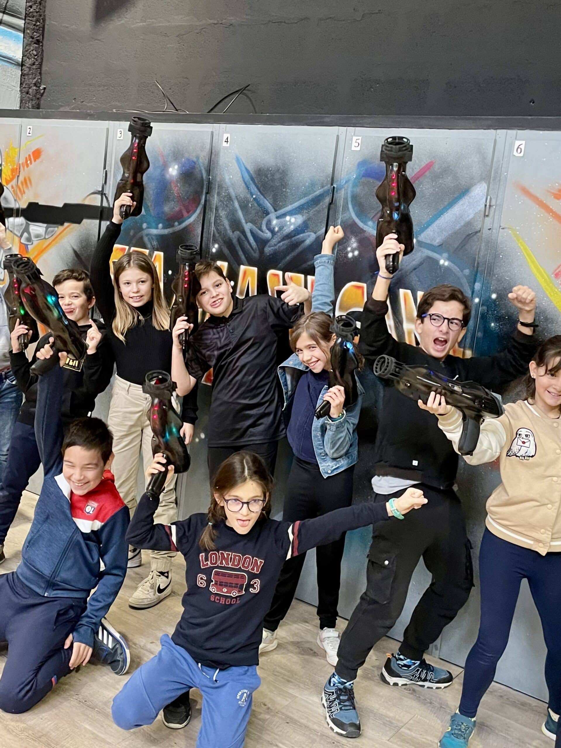 Enfants joyeux posant avec des pistolets laser tag devant des graffitis dans un centre de loisirs laser game.