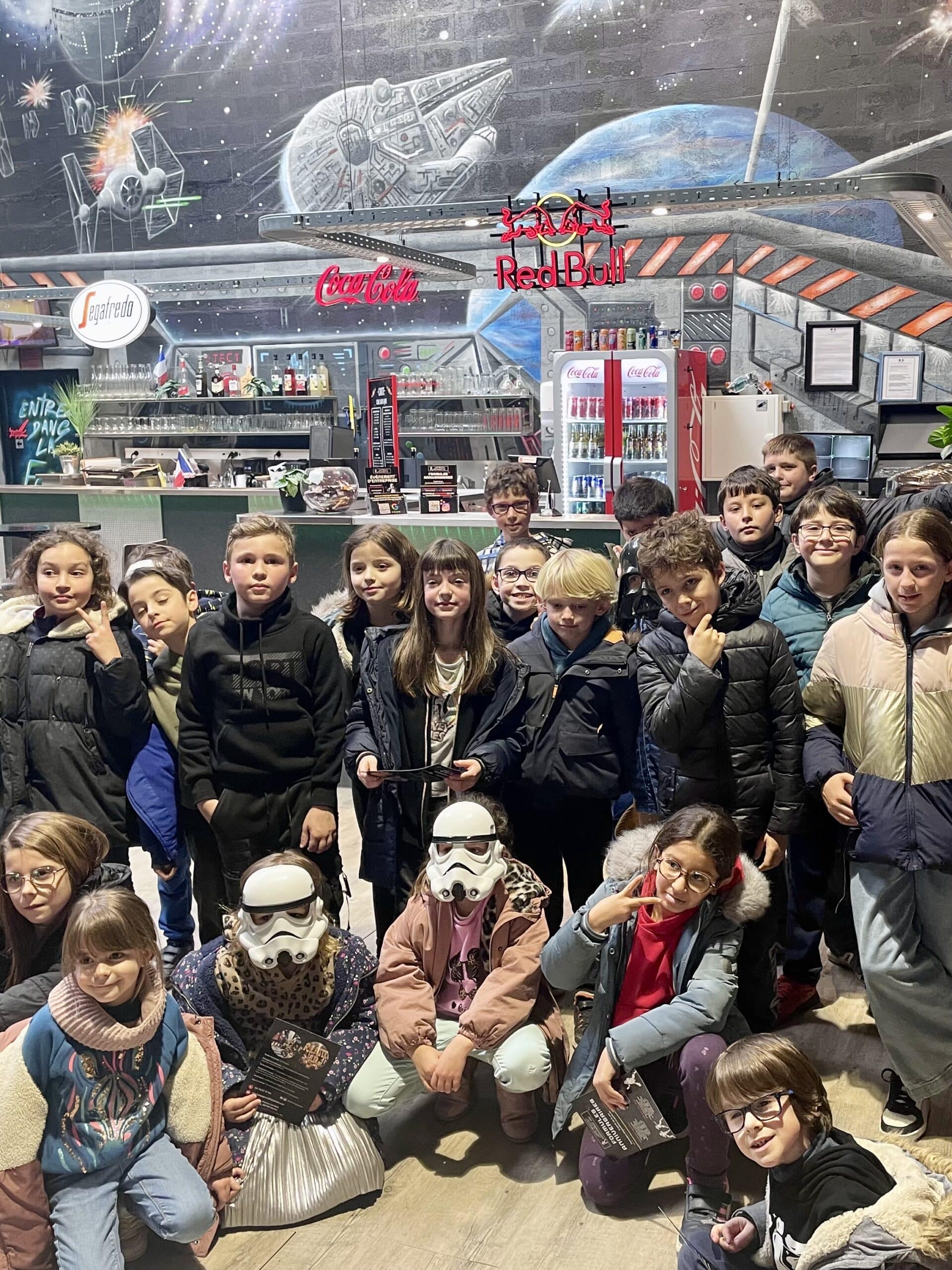 Groupe d'enfants souriants dans un centre de loisirs spatial avec fresque Star Wars, logos Coca-Cola et Red Bull.