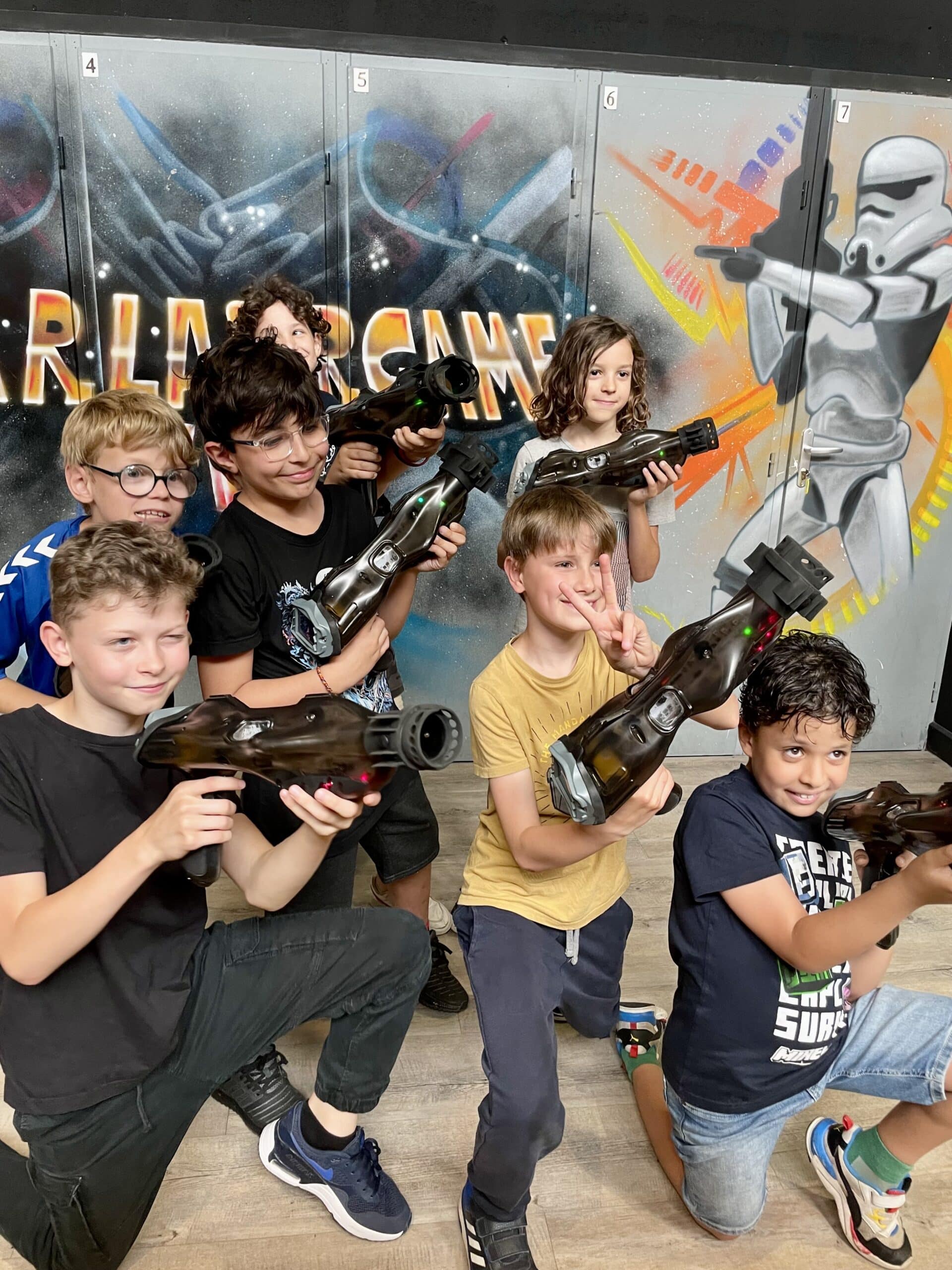 Enfants souriants posant avec des pistolets laser devant un décor Laser Game et un Stormtrooper.