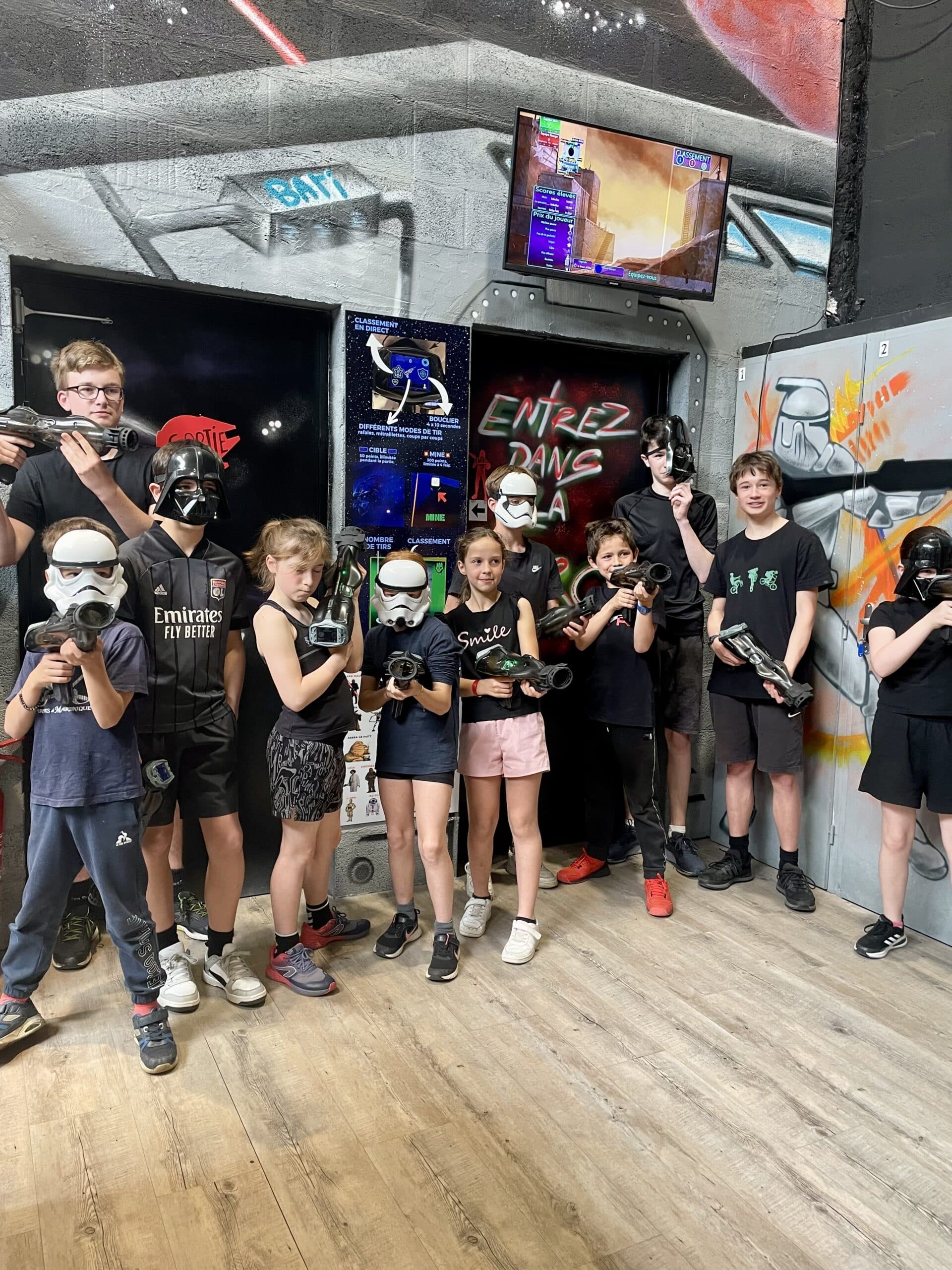 Groupe d'enfants avec masques Star Wars et pistolets laser posant dans une salle de laser game avec graffiti.