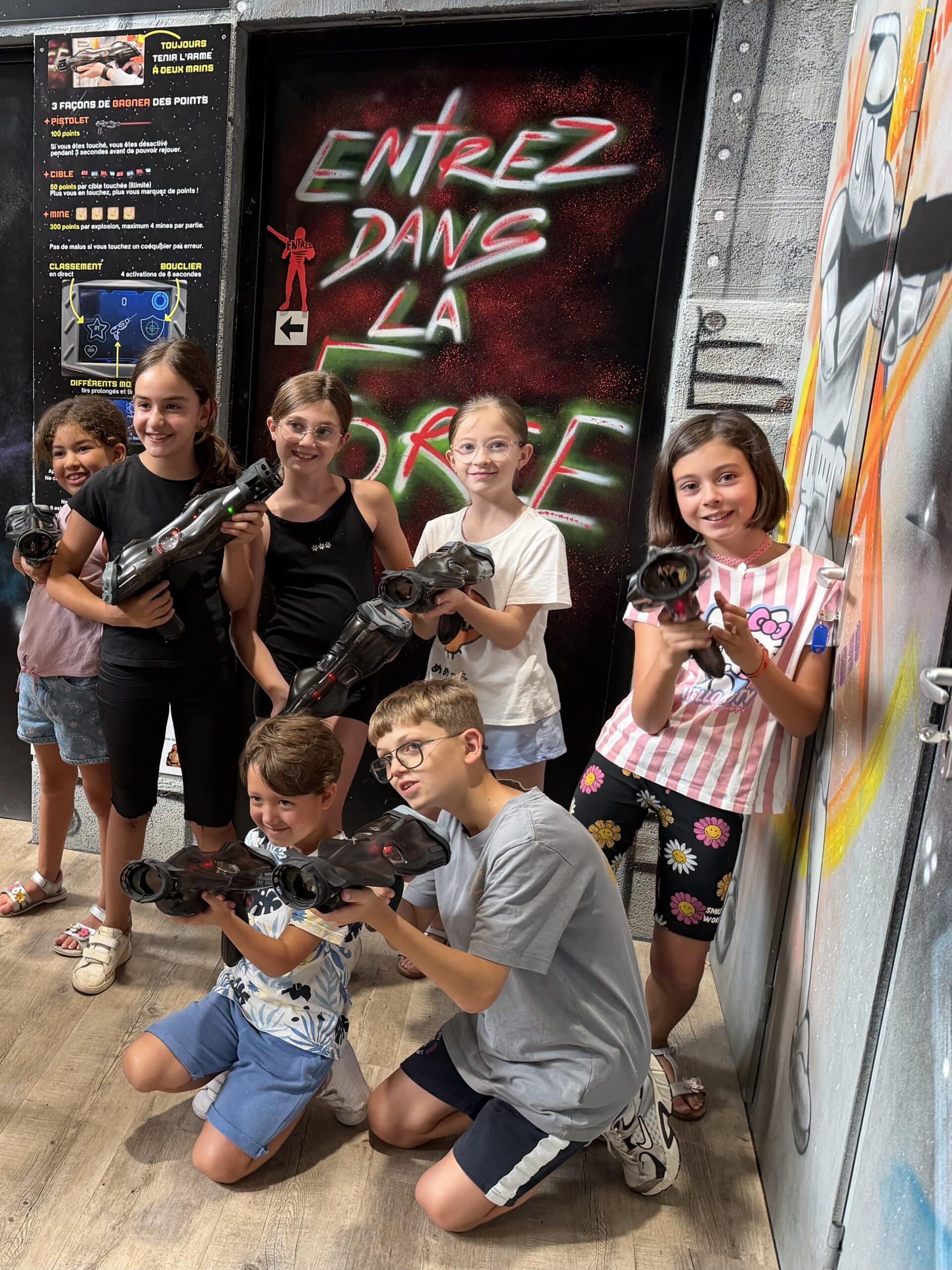 Groupe d'enfants souriants avec pistolets laser devant une porte taguée Entrez dans la Force au laser tag.