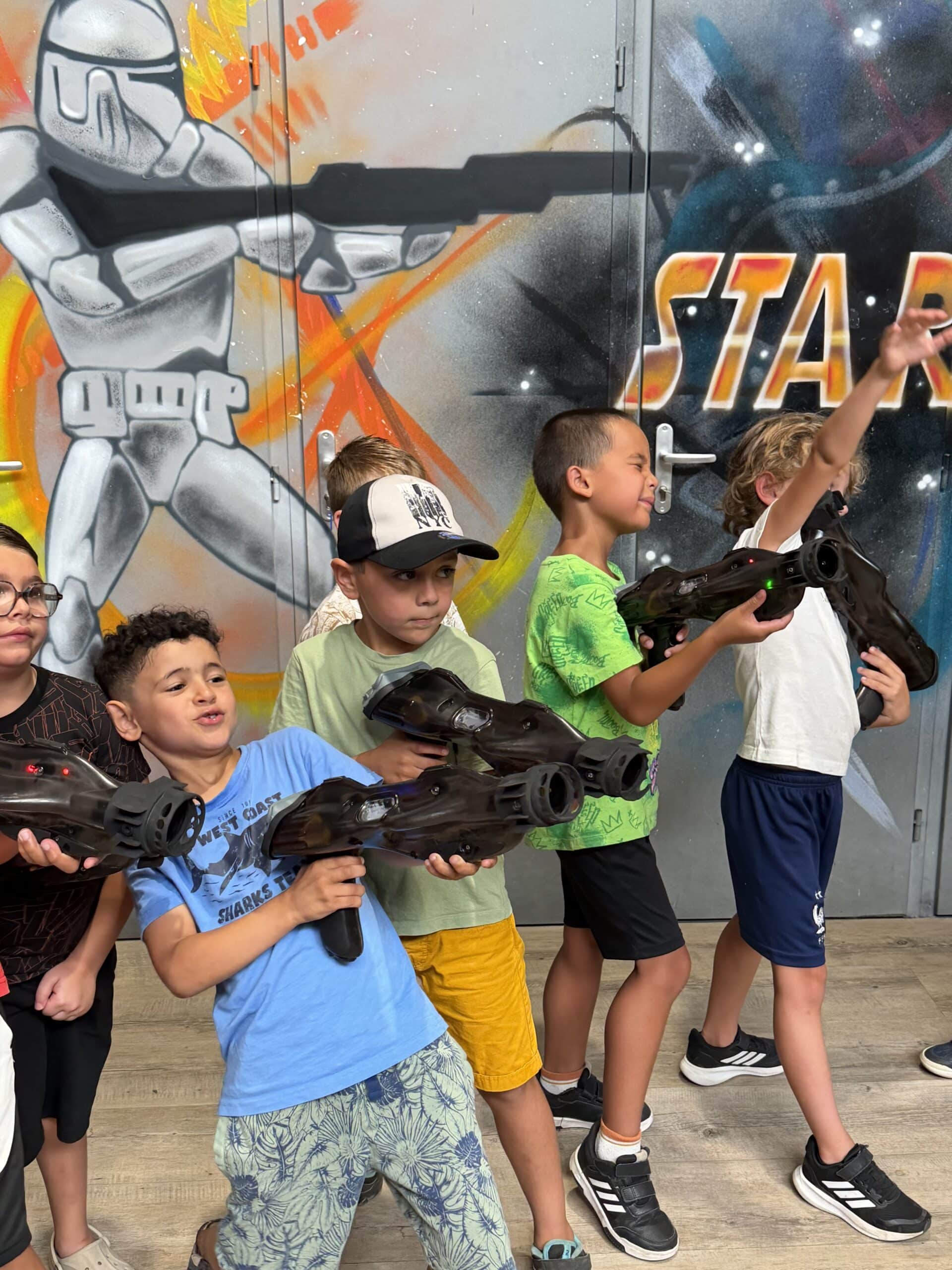 Enfants jouant au laser tag devant une fresque Star Wars, pistolets futuristes en main. Moment de jeu et d'aventure.