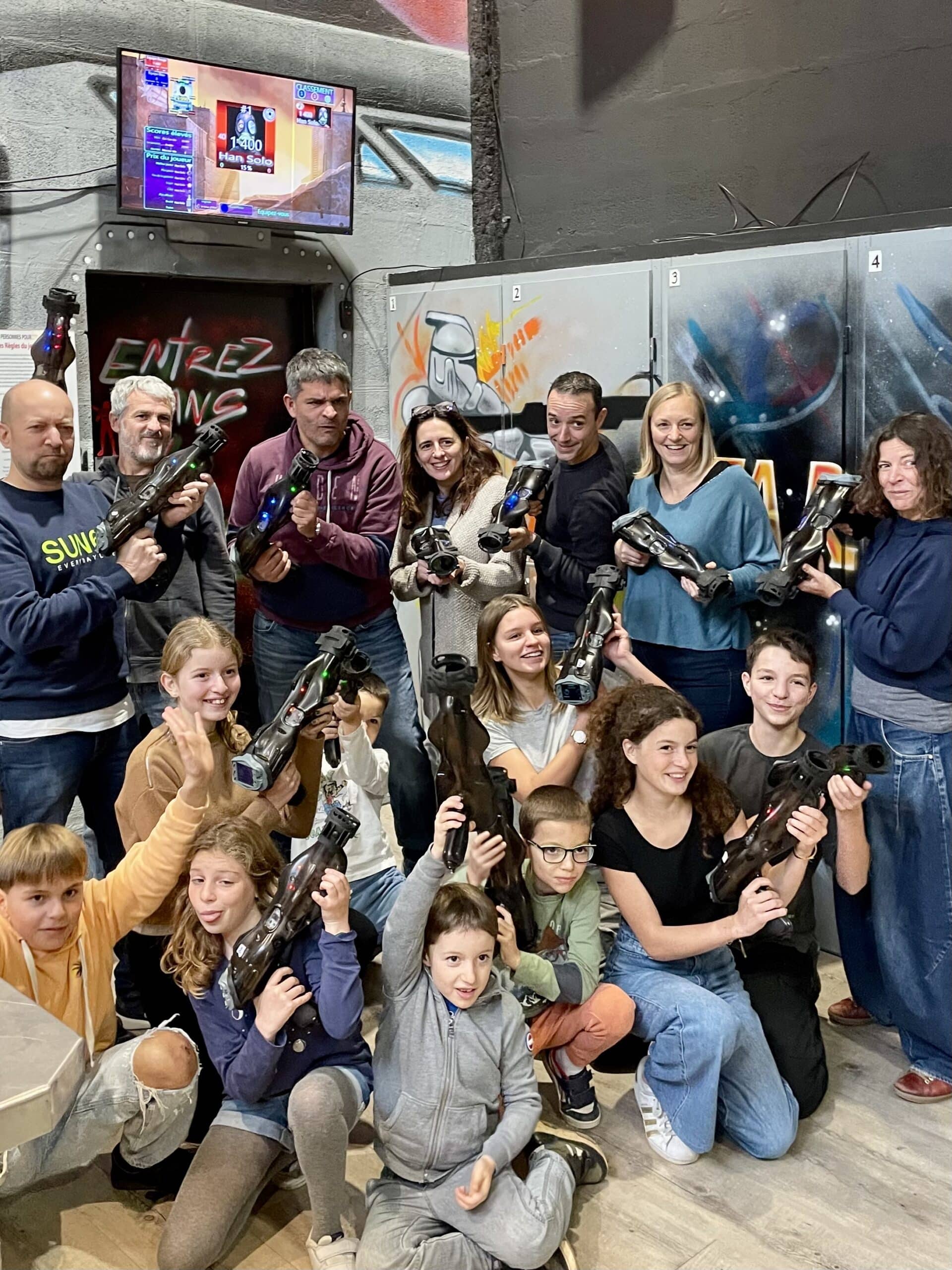 Groupe souriant au laser tag avec blasters devant un décor Star Wars et un écran de scores Han Solo.