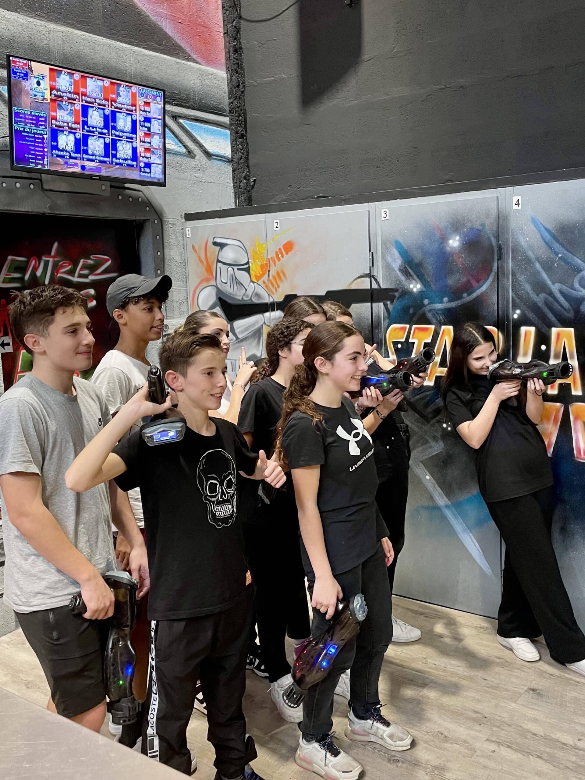 Ados souriants avec pistolets laser tag posant devant un mur Star Wars et un tableau de scores électronique.