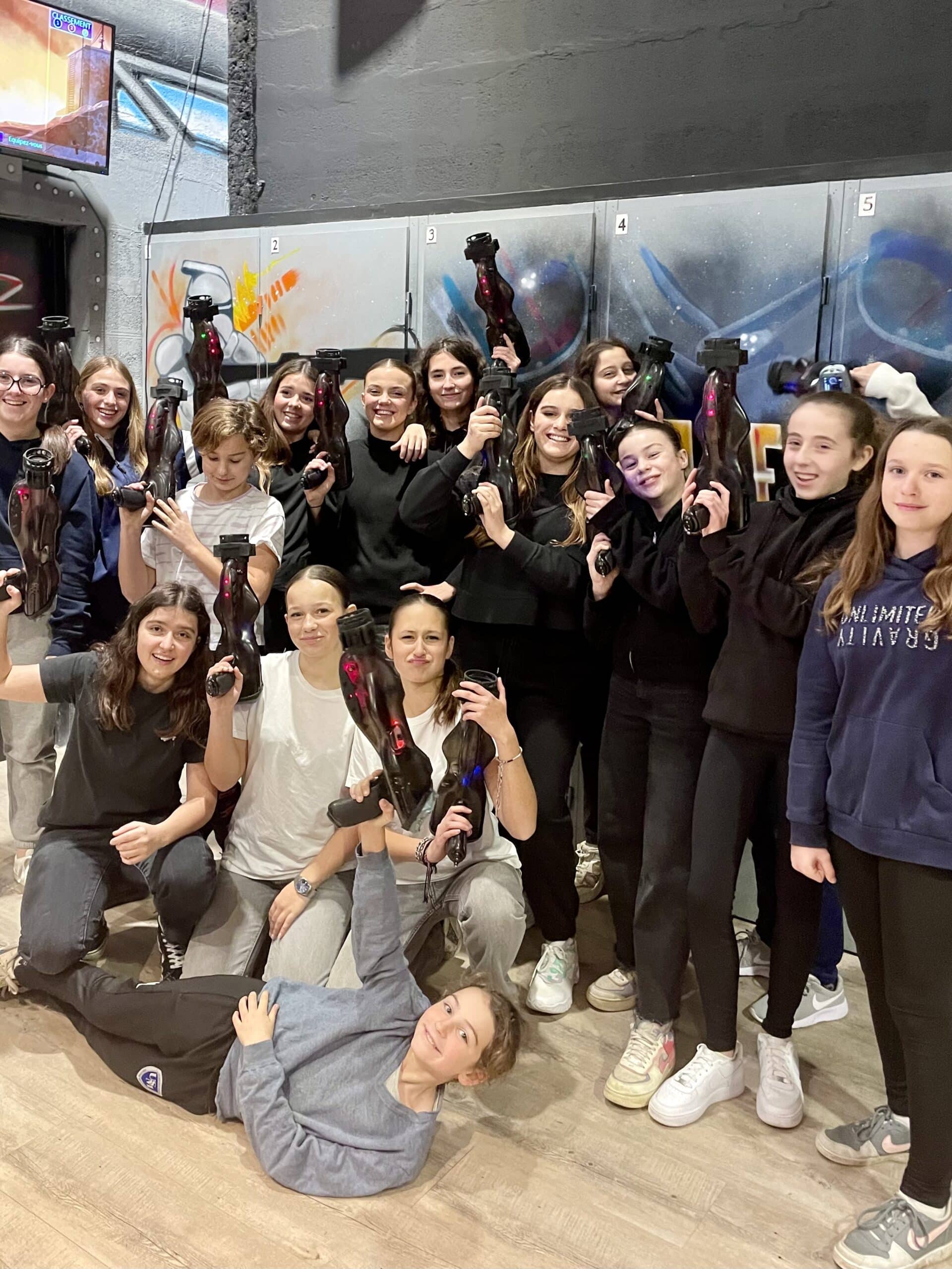 Groupe de jeunes filles souriantes avec des pistolets laser tag dans un centre de jeux devant des graffitis.