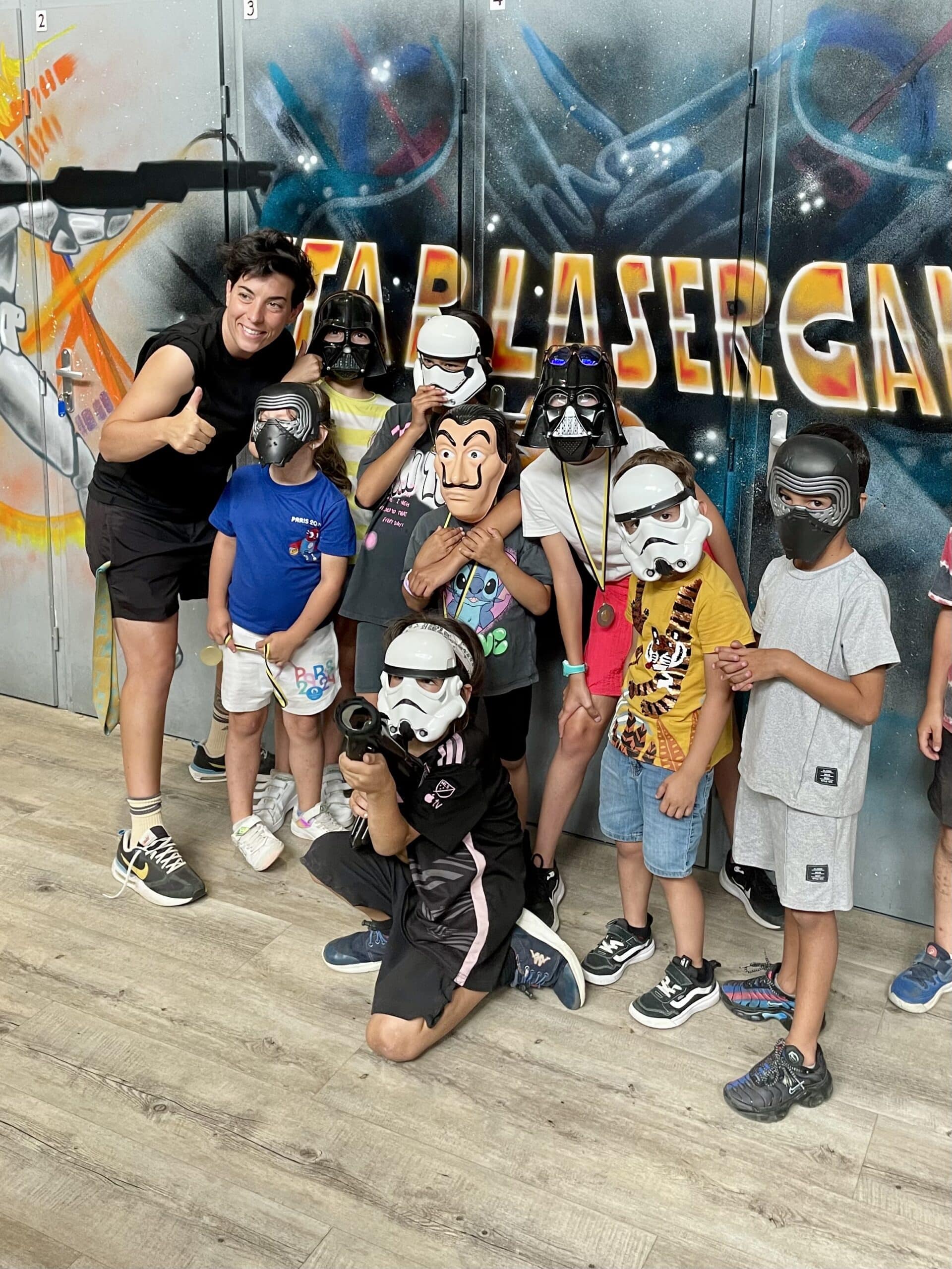 Enfants en masques Star Wars et adulte devant l'enseigne STAR LASER GAME, ambiance joyeuse de sortie de groupe.