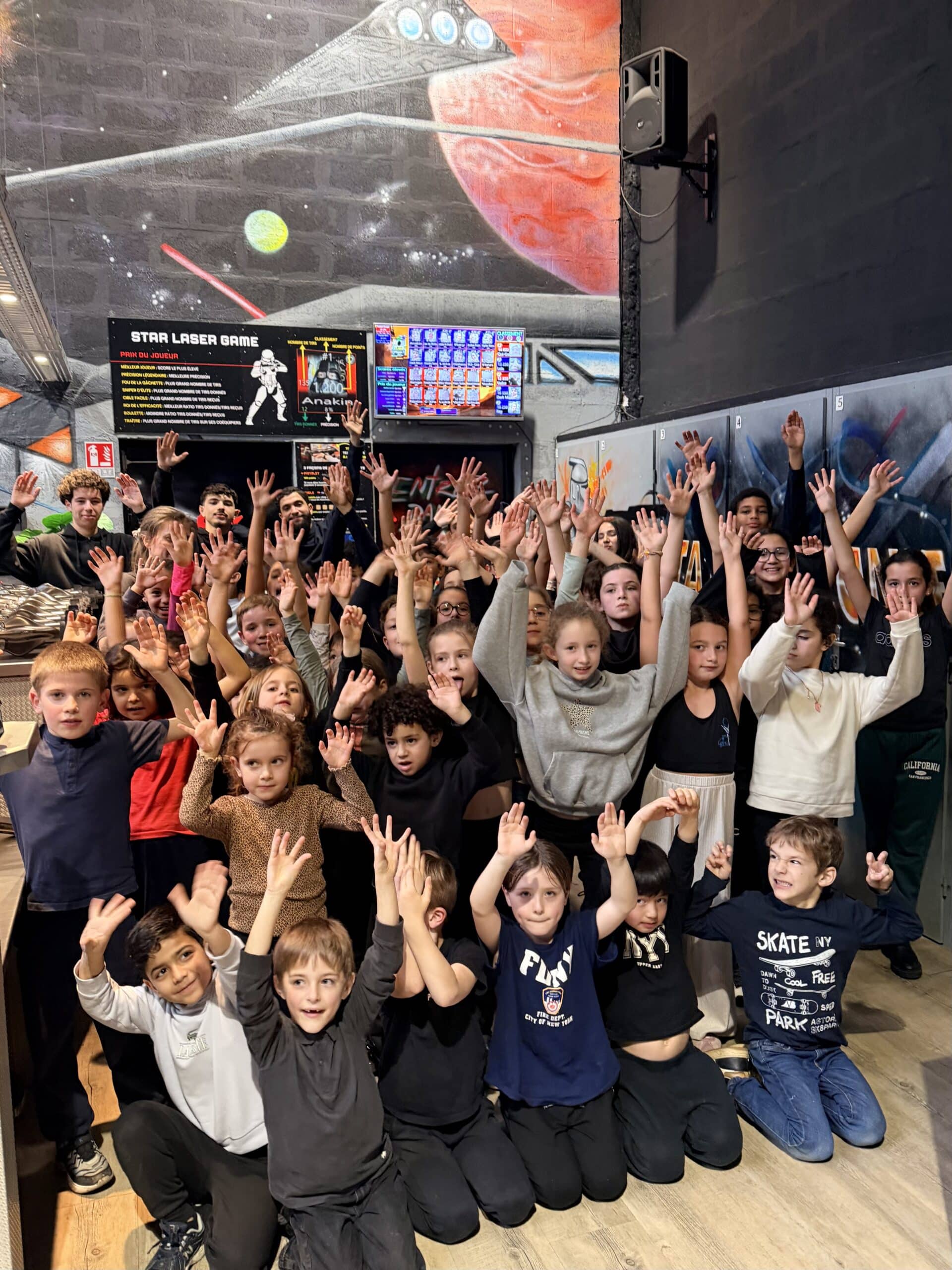 Groupe d'enfants enthousiastes les mains levées au Star Laser Game devant une fresque spatiale colorée.