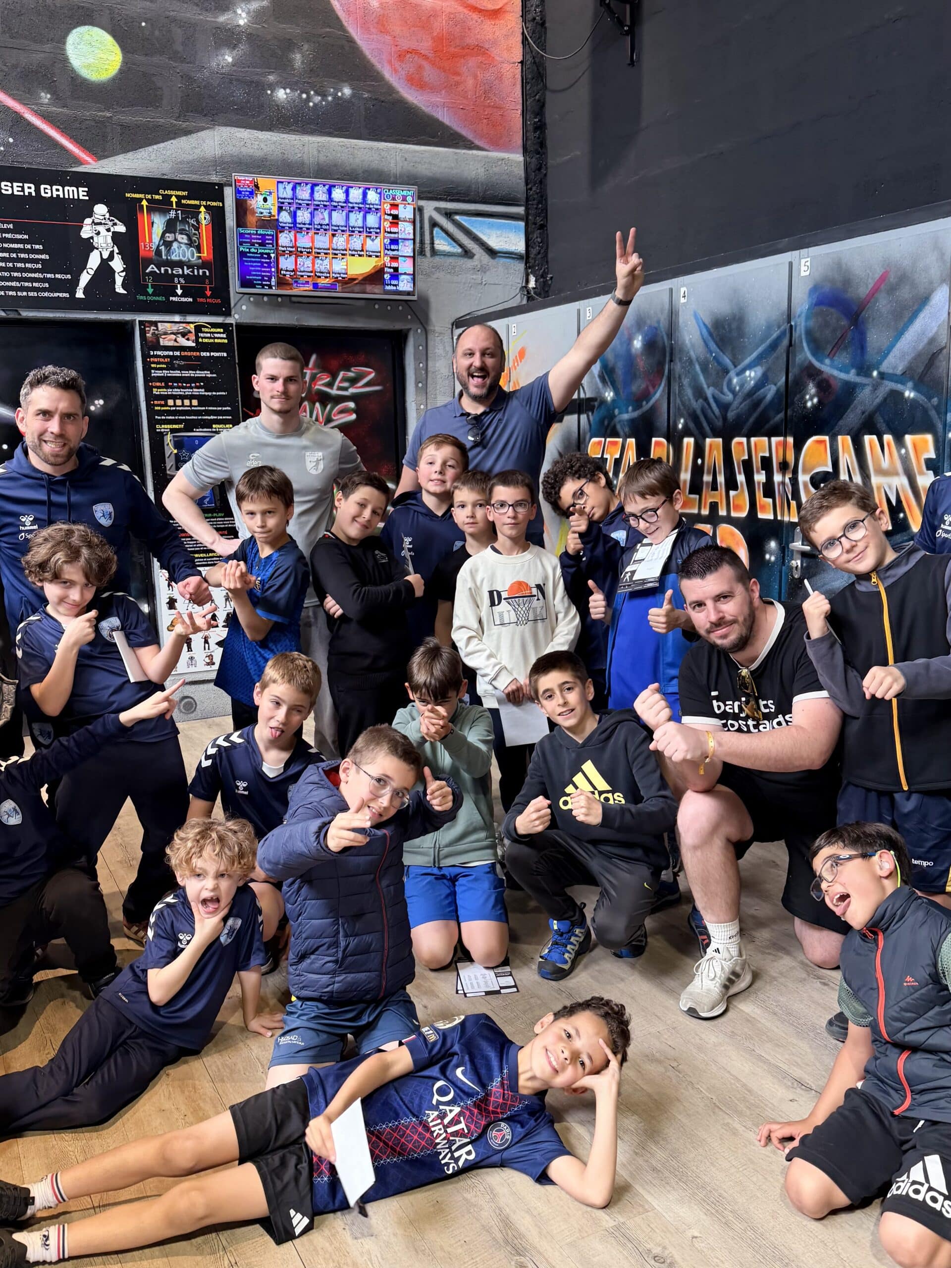 Enfants et adultes posant joyeusement au Star Lasergame devant un décor spatial et un tableau de scores.